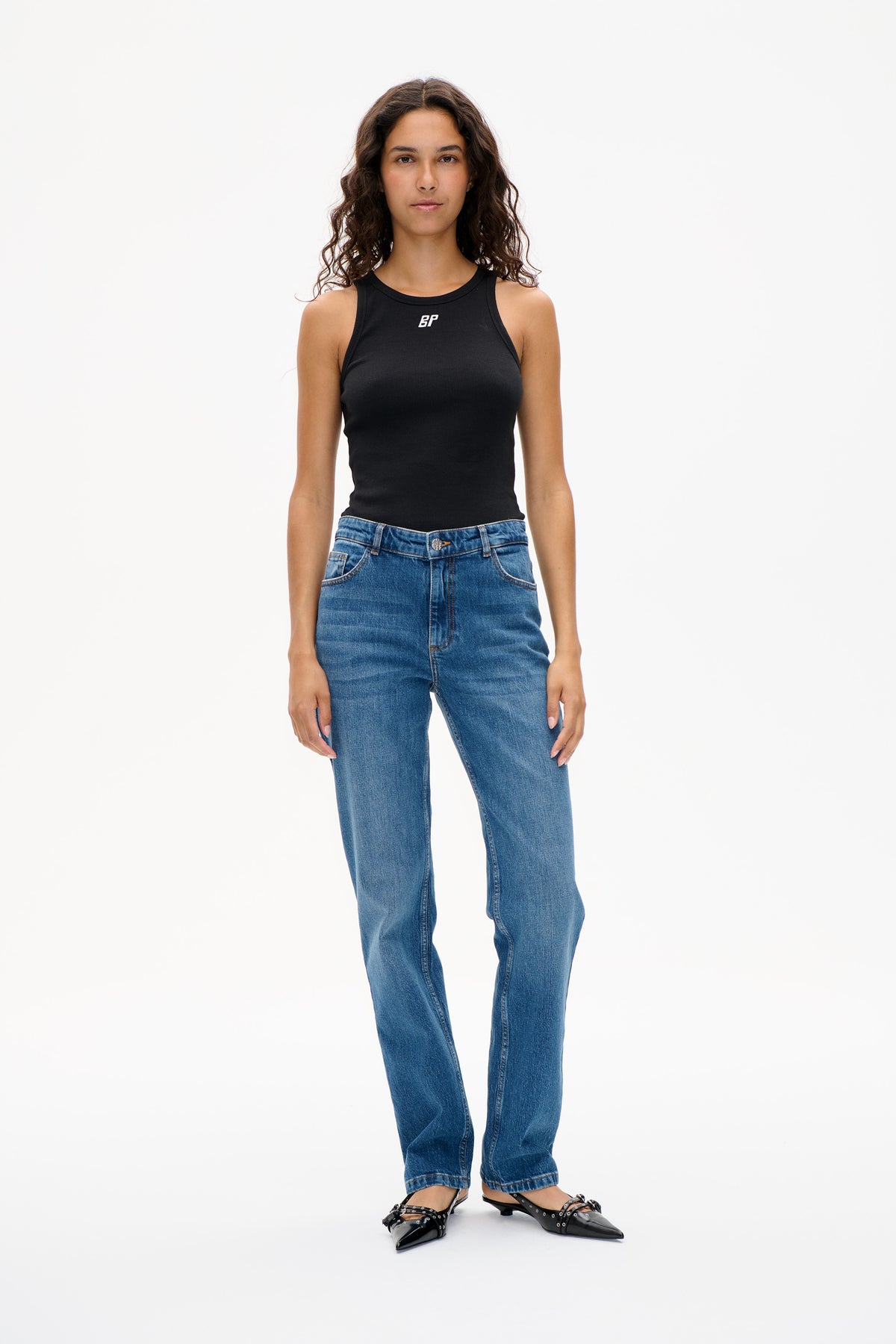 Vooraanzicht van een zwarte mouwloze geribde top met klein wit borstlogo, gestyled met blauwe jeans.