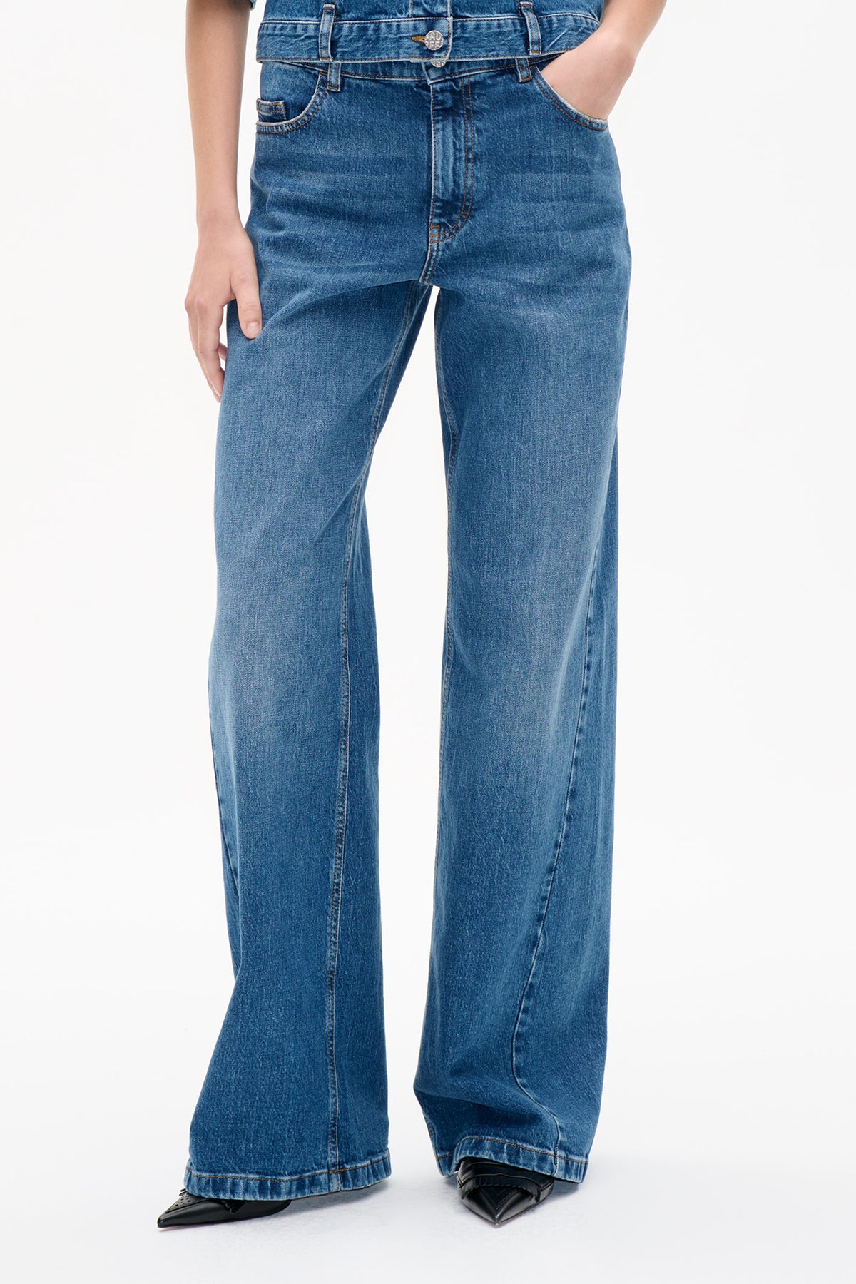 Front detail of faded blue wide-leg jeans, showing the button closure, belt loops, curved pockets and contrast stitching.