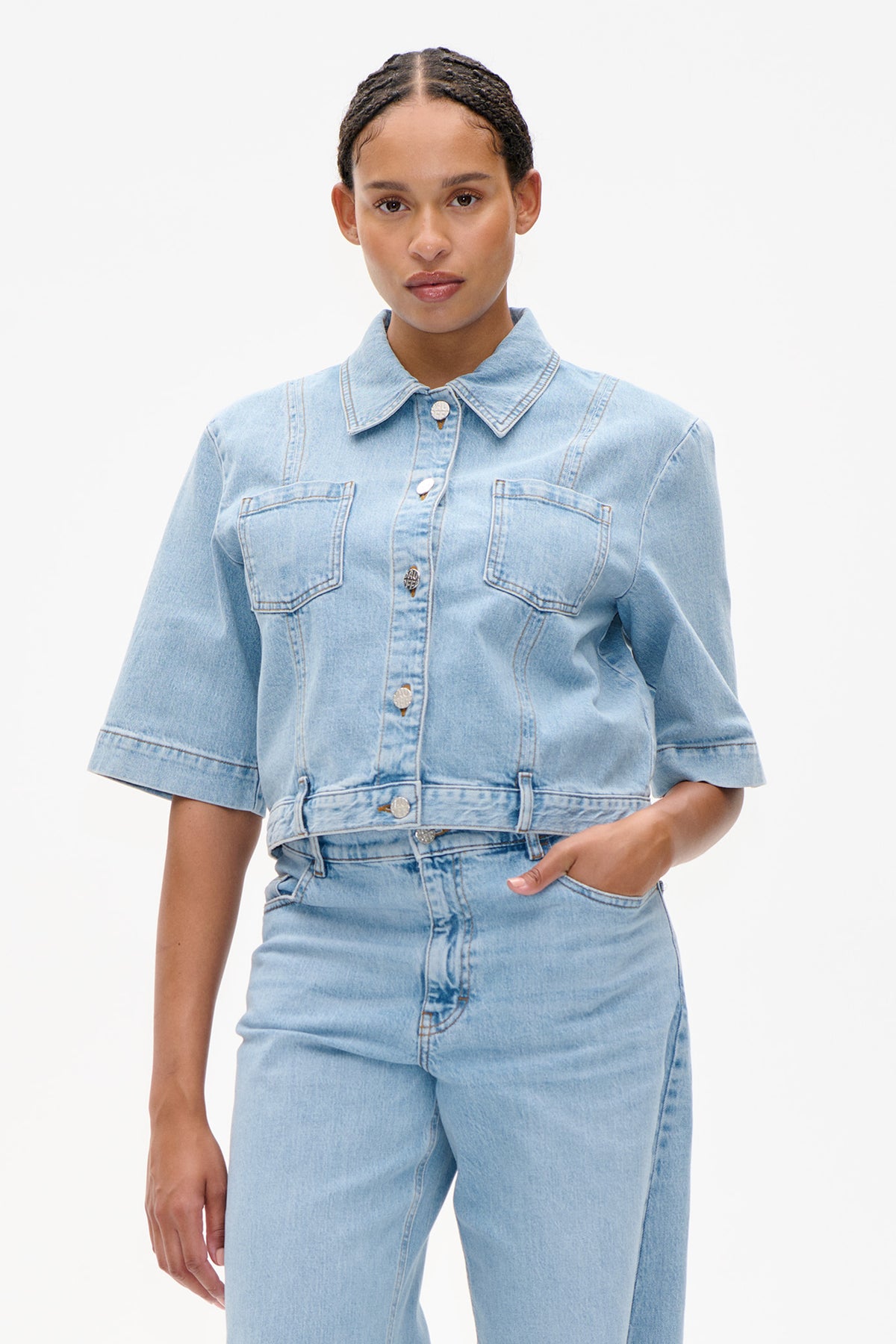 Front detail of a light-wash denim jacket with short sleeves, an oversized collar, button fastening and two chest pockets, worn with matching jeans.