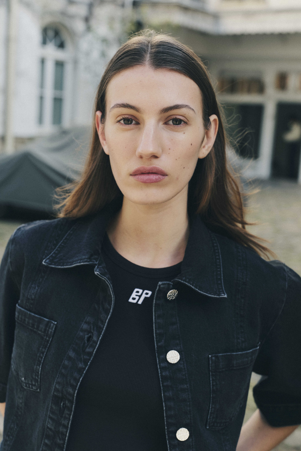Close-up portrait of a model wearing a dark denim jacket with contrast stitching over a black T-shirt with white lettering.