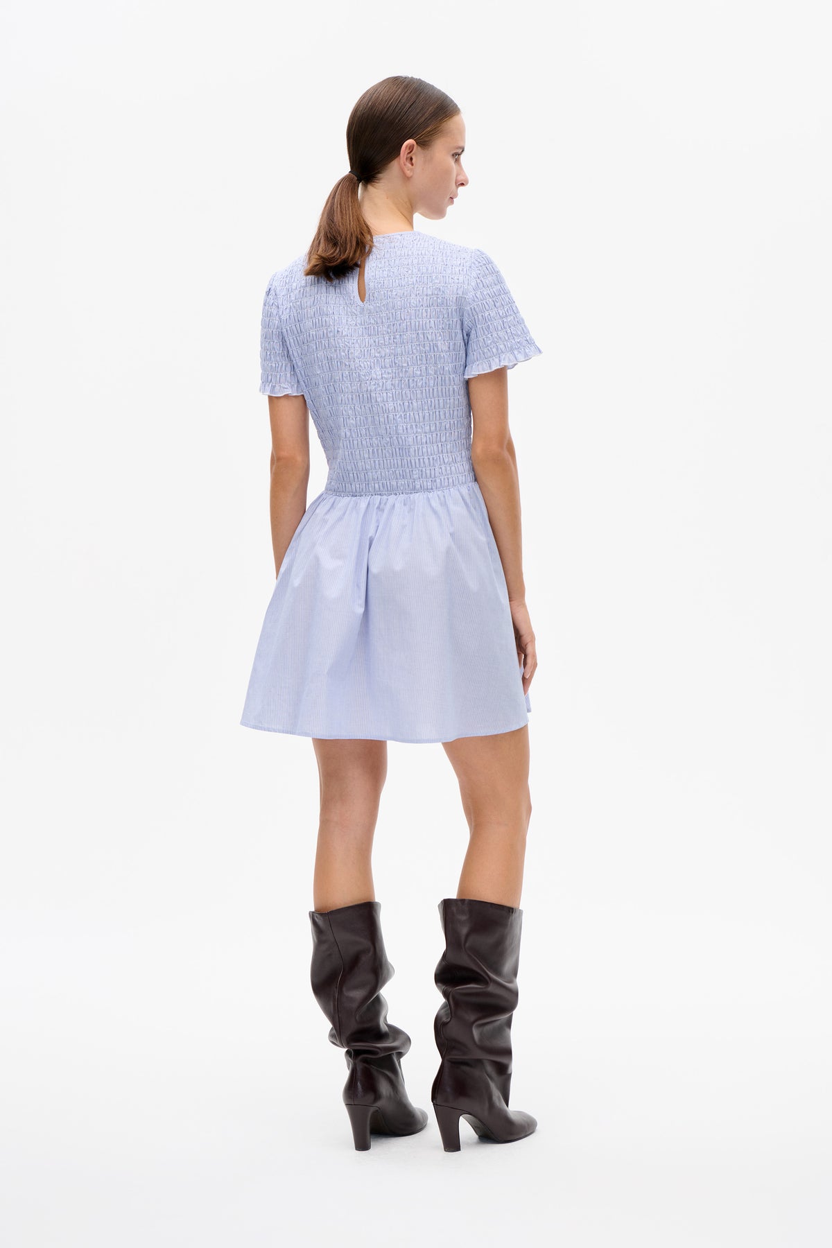 Model turned away wearing a pale blue short-sleeved dress with a smocked bodice, ruffled sleeves and a back keyhole opening.