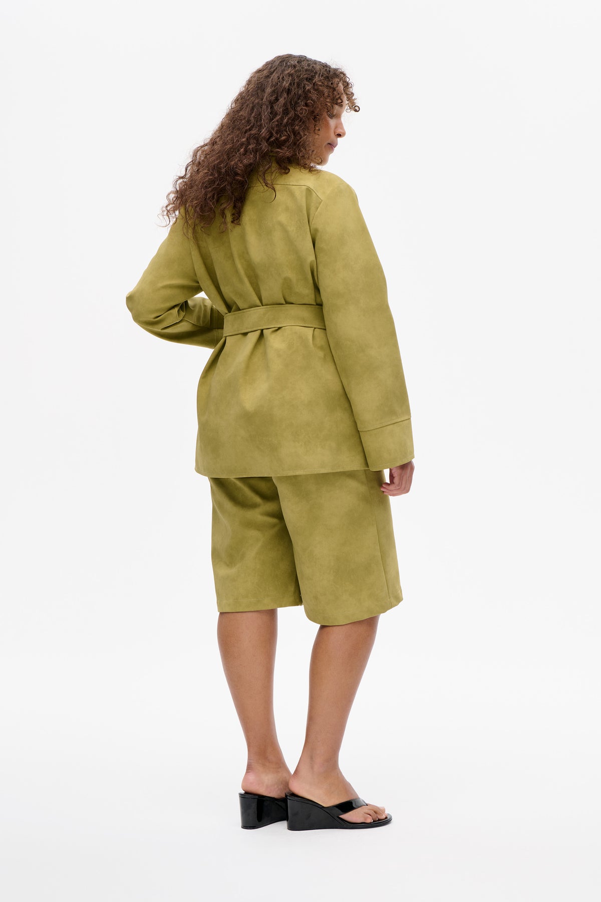 Model in a back three-quarter view wearing an olive-green belted jacket and matching knee-length shorts.