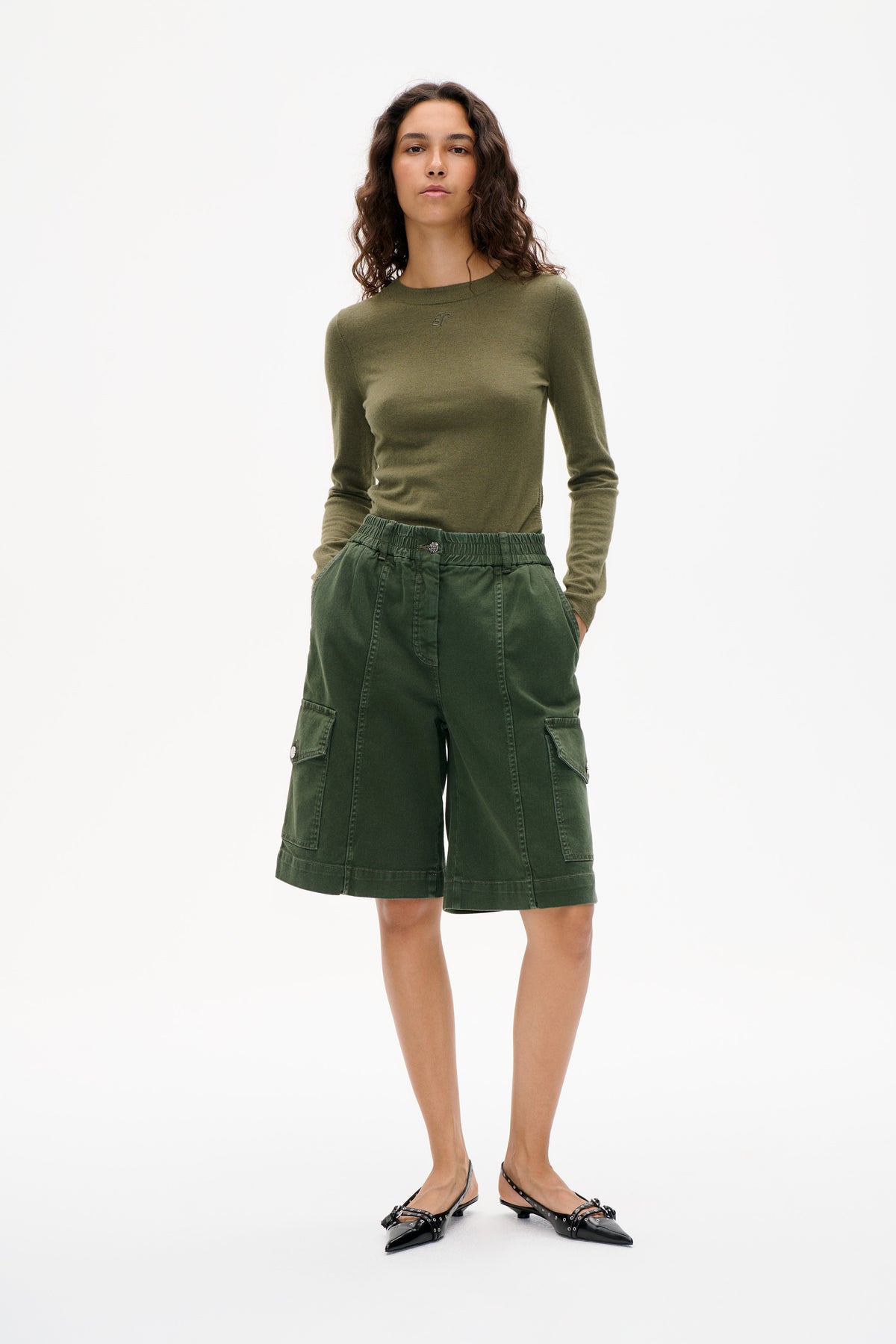 Front view of a model wearing an olive long-sleeve top with a small chest logo and dark green cargo shorts with flap pockets.