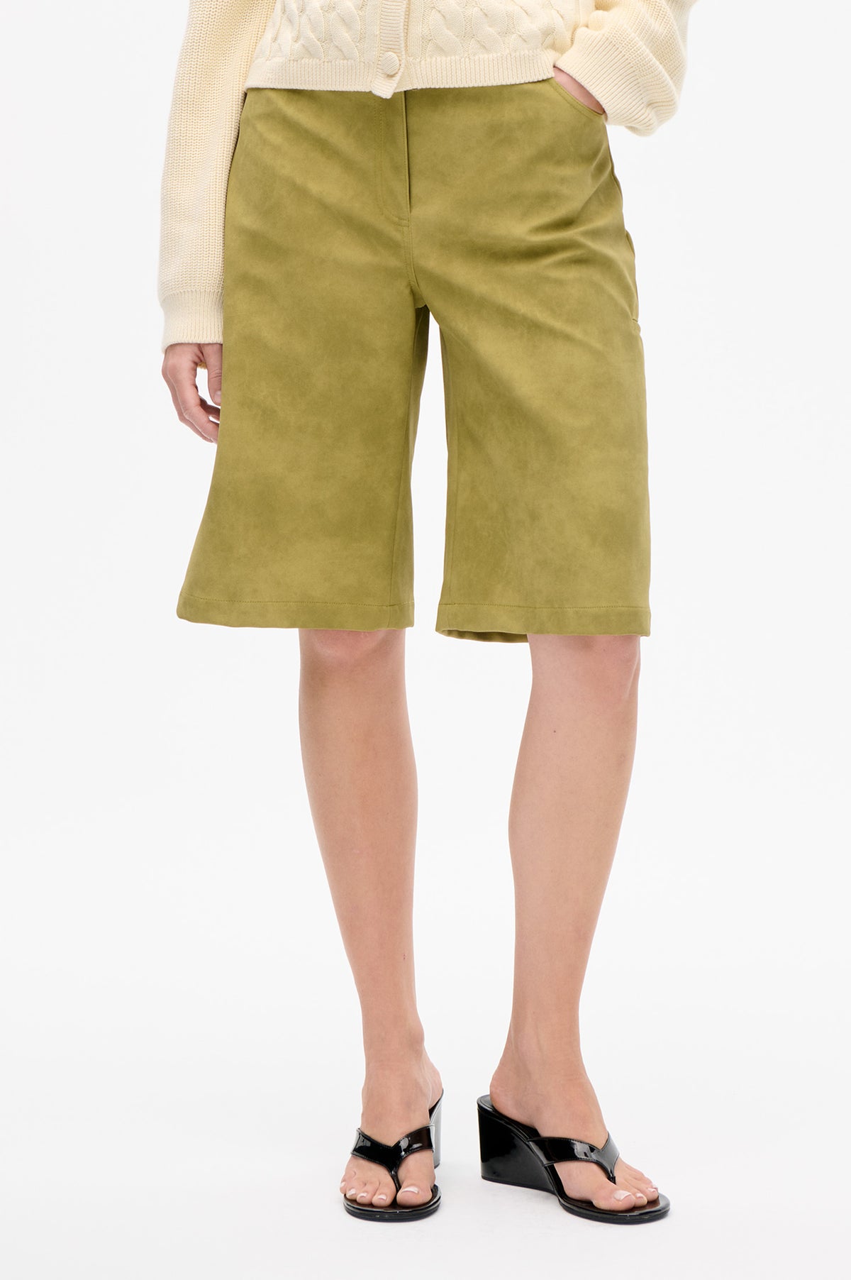 Detailaufnahme vorne: olivgrüne, knielange Shorts mit weitem Bein und schrägen Taschen, kombiniert mit einem cremefarbenen Cardigan im Zopfmuster.