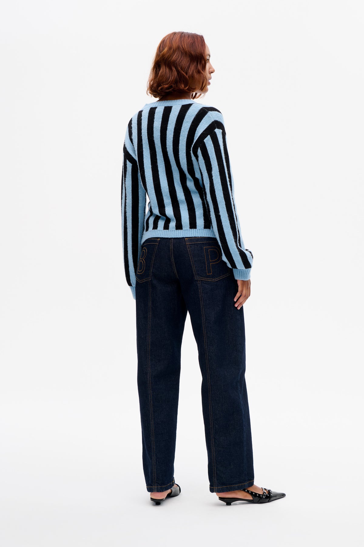 Model shown from the back wearing a light blue and black vertically striped knit sweater with dark wide-leg jeans.