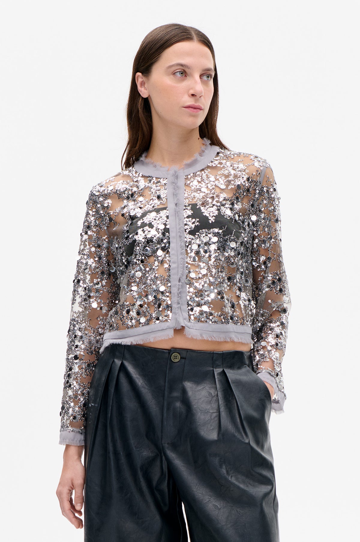 Front view of a sheer cropped blouse with silver and black sequins, long sleeves, and pale grey frayed trim