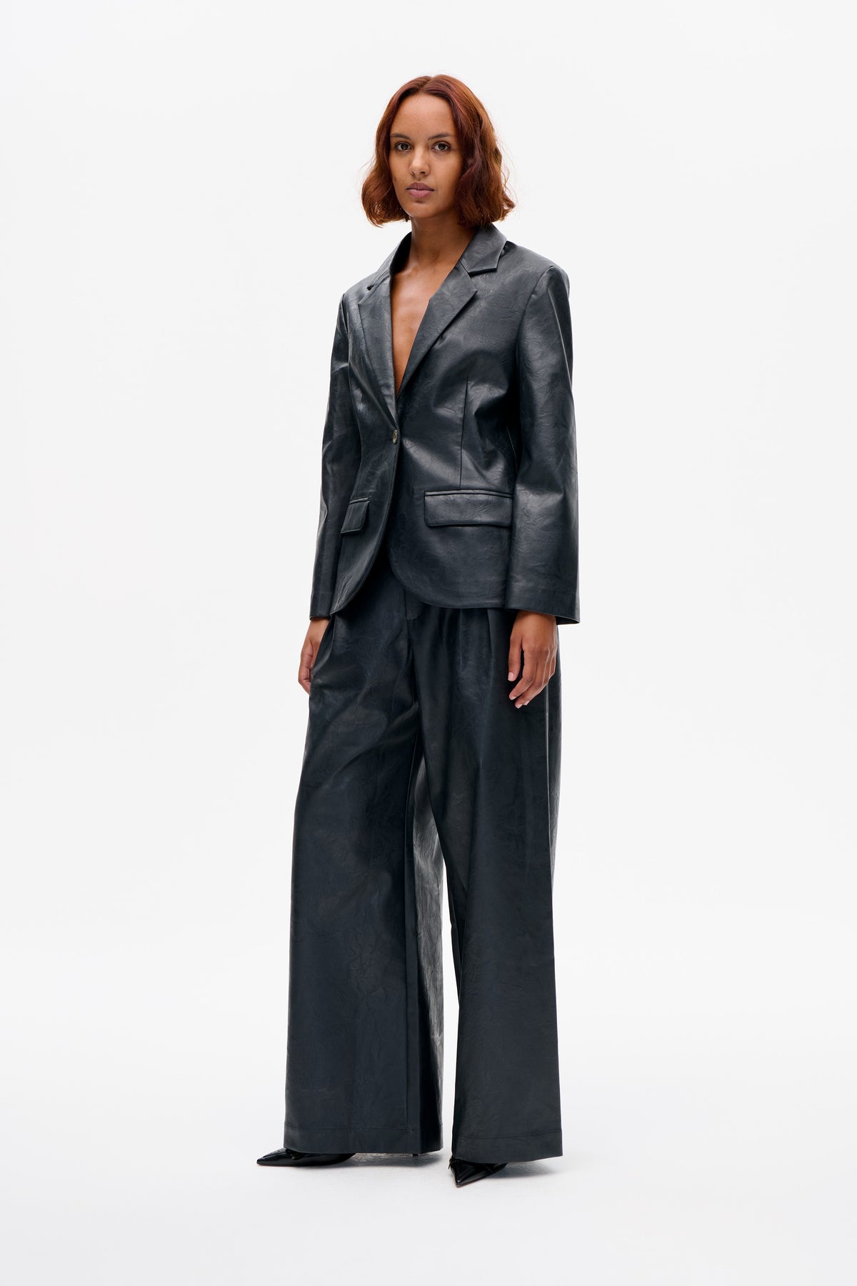 Model wearing a dark charcoal crinkled blazer with notched lapels and flap pockets, paired with matching wide-leg trousers, front view.