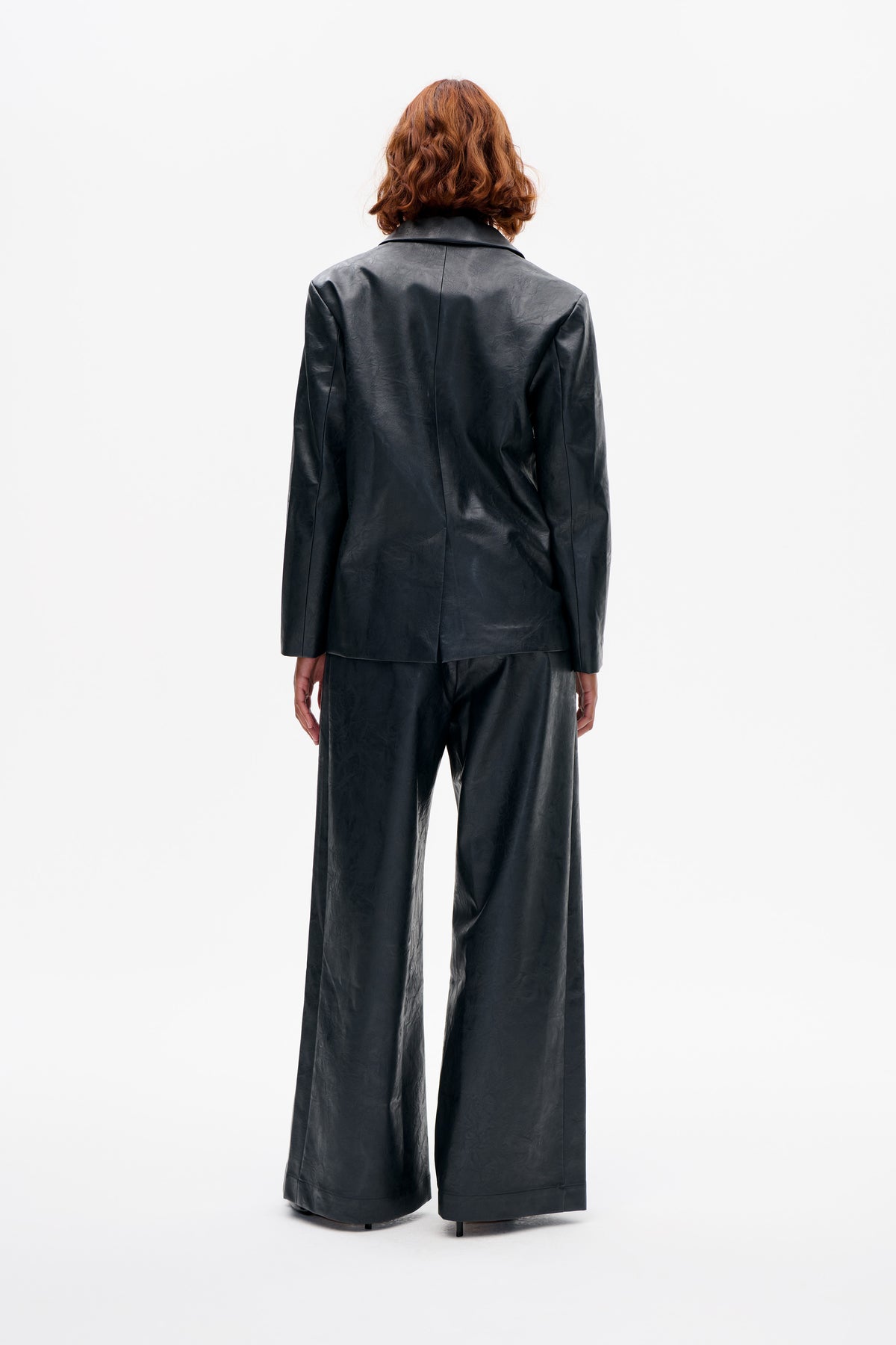 Back view of a model wearing a black notched-lapel jacket and matching wide-leg trousers with a subtle sheen.