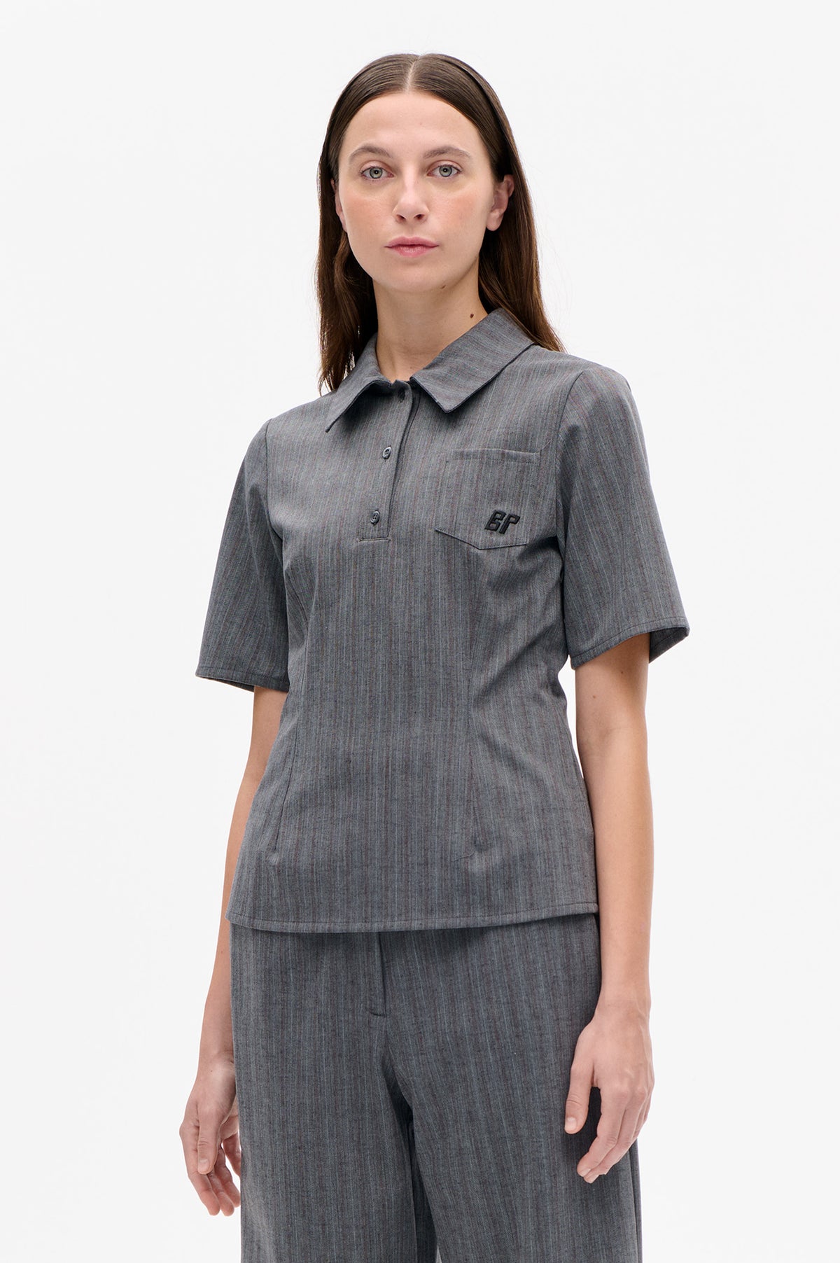 Front view of a grey subtly pinstriped short-sleeve button-up shirt with pointed collar, chest pocket and black monogram, paired with matching trousers.