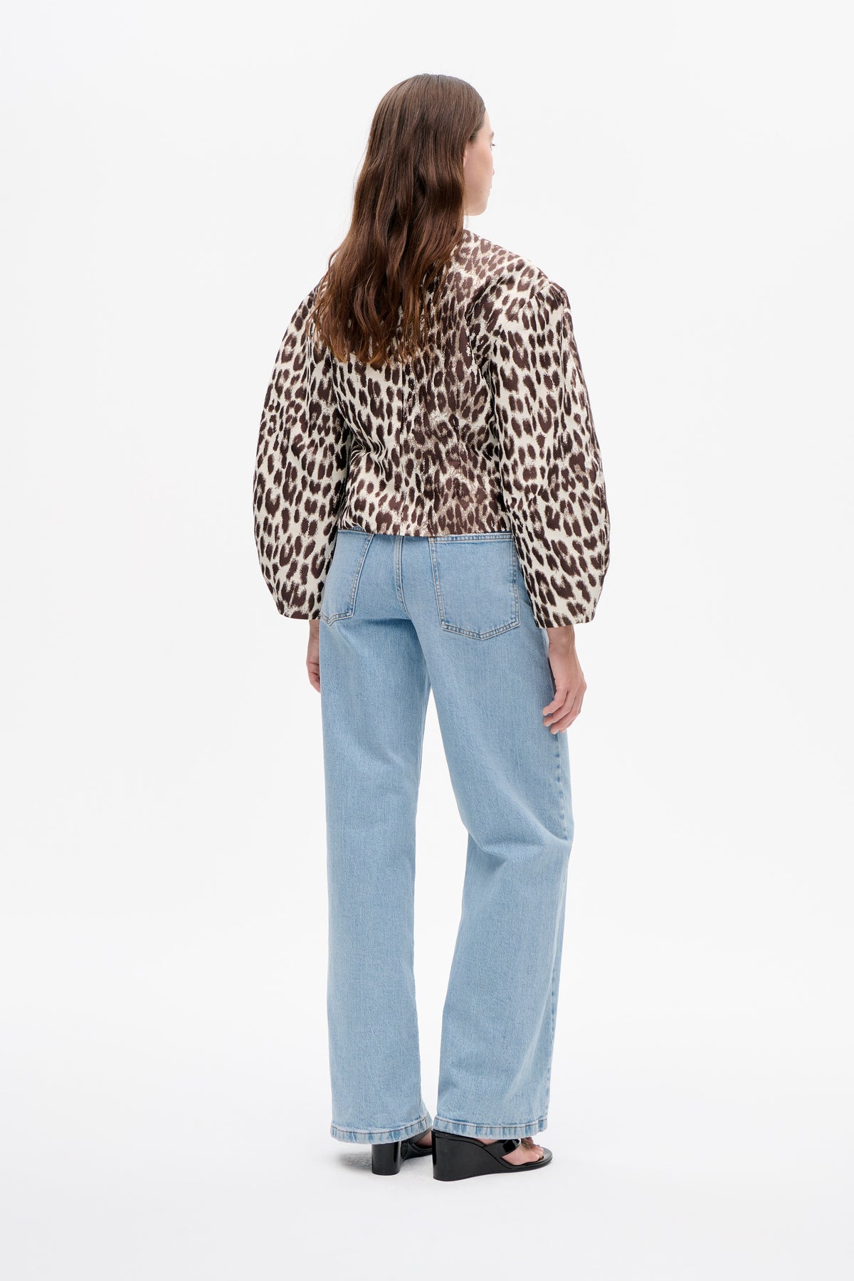 Back view of a model wearing a brown and cream animal-print long-sleeved blouse with light blue wide-leg jeans.