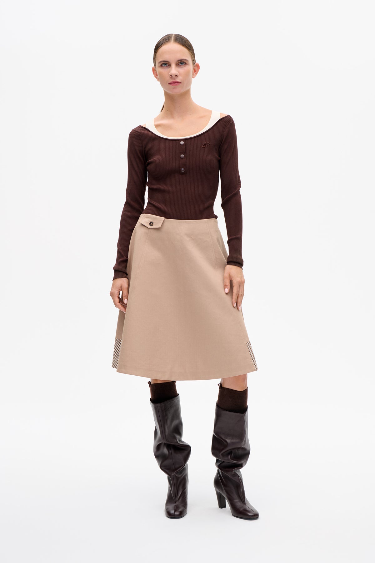 Model wearing a dark brown ribbed button-front top with a wide neckline and a beige A-line skirt with gingham side panels.