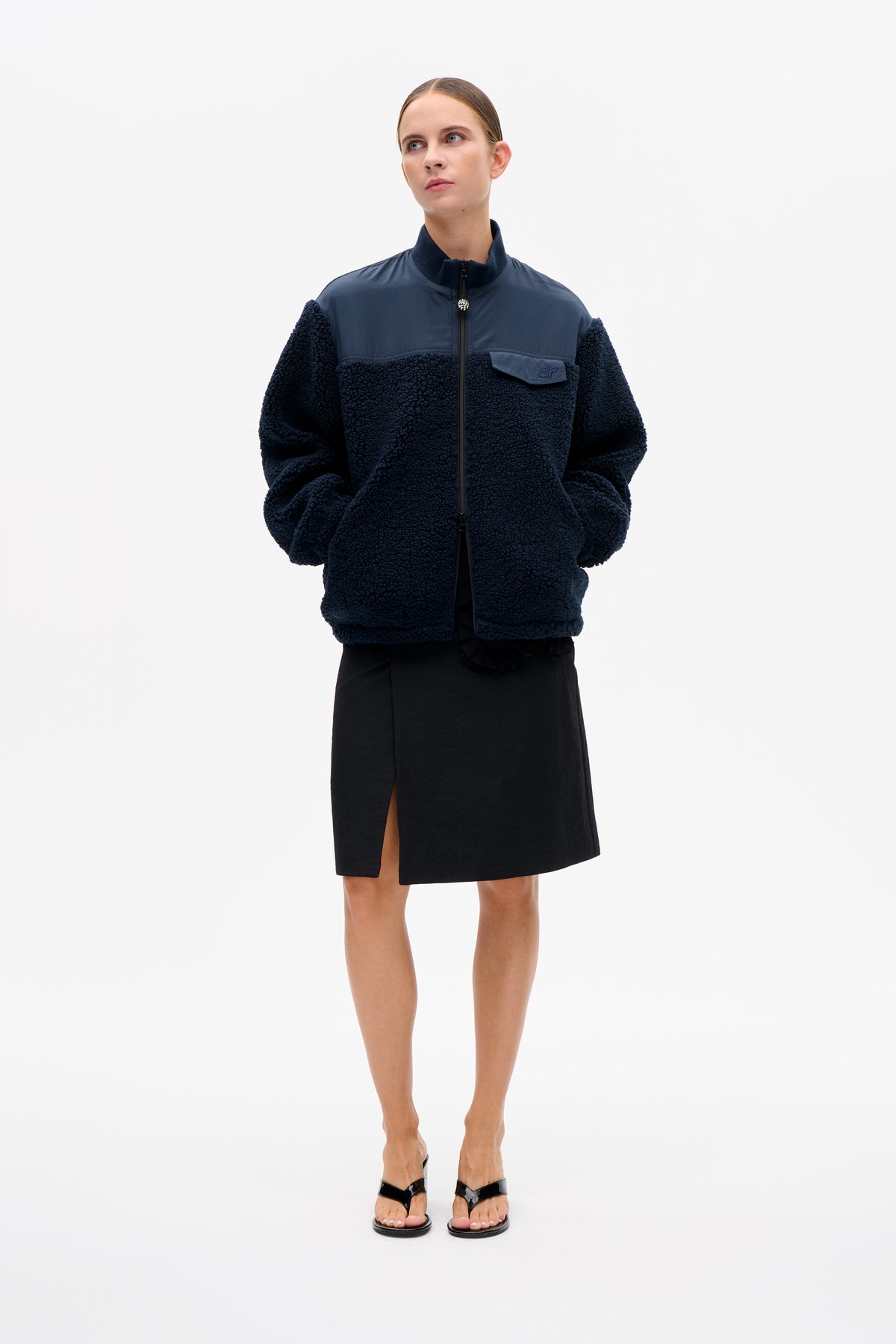 Front view of a model wearing a navy textured zip-up jacket with a smooth blue upper panel, high collar and flap chest pocket.