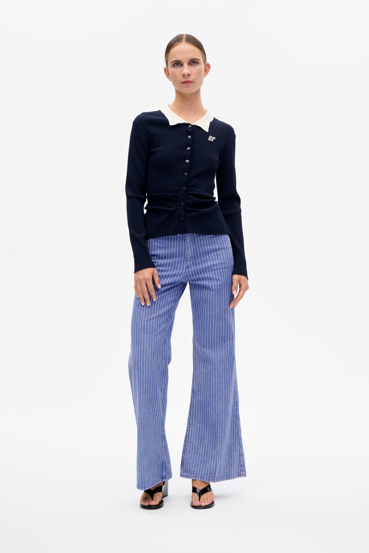 Model wearing a navy ribbed button-front cardigan with a white collar and blue wide-leg trousers with fine vertical stripes.