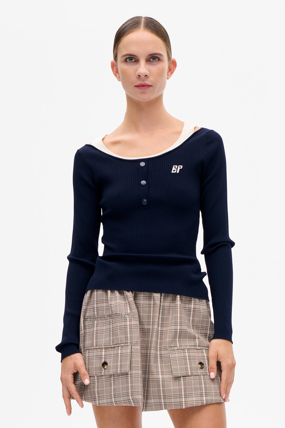 Front view of a navy ribbed long-sleeve top with a wide neckline, snap buttons and white BP emblem, paired with beige plaid shorts.