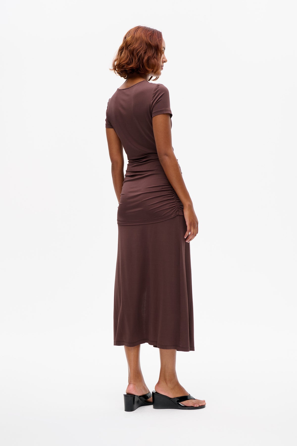 Model draagt een mauve midi-jurk met korte mouwen, een gerimpelde taille en zijnaad, gezien van achteren en opzij.
