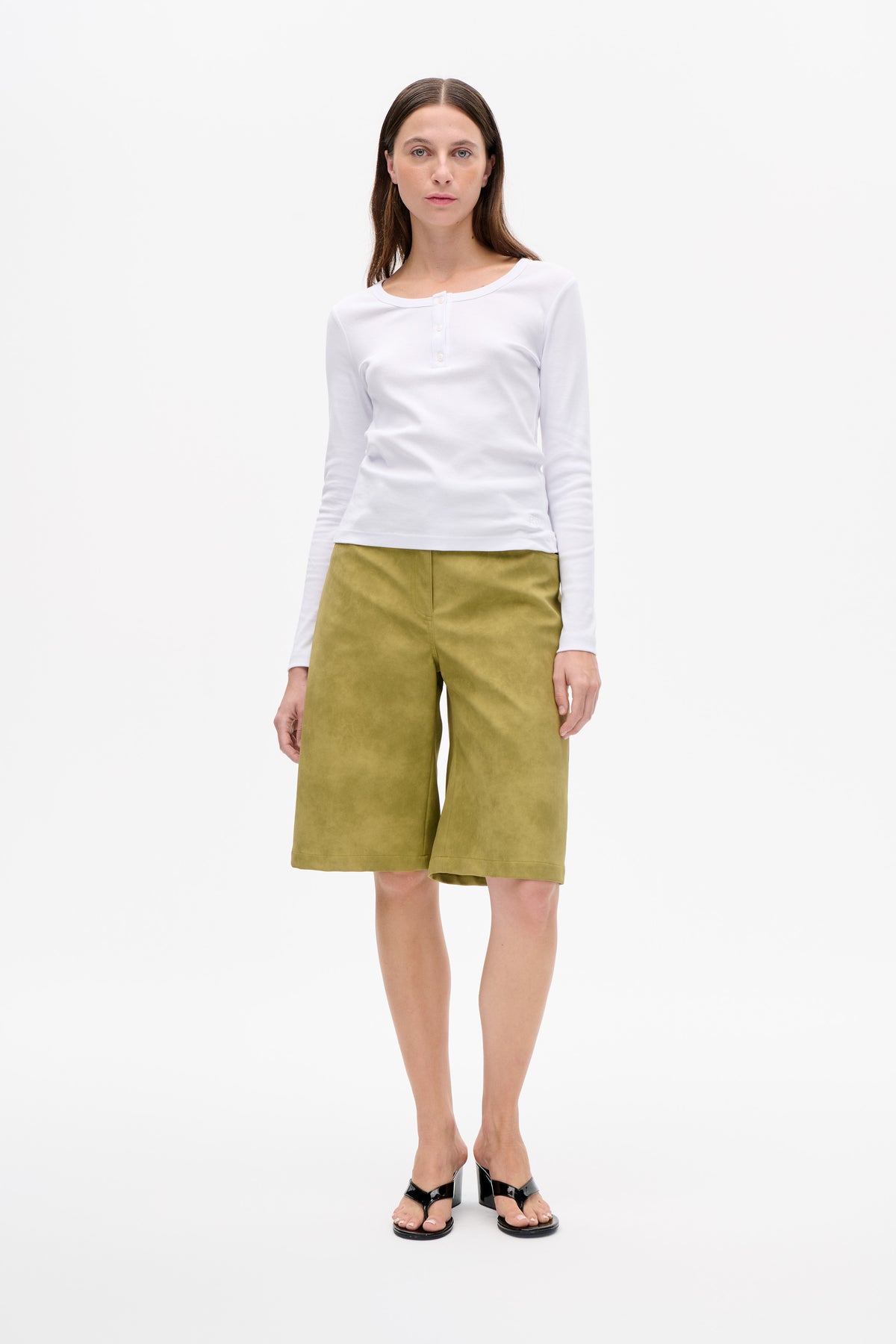 Front view of a model wearing a white long-sleeved top with a button placket and olive green knee-length wide-leg shorts.