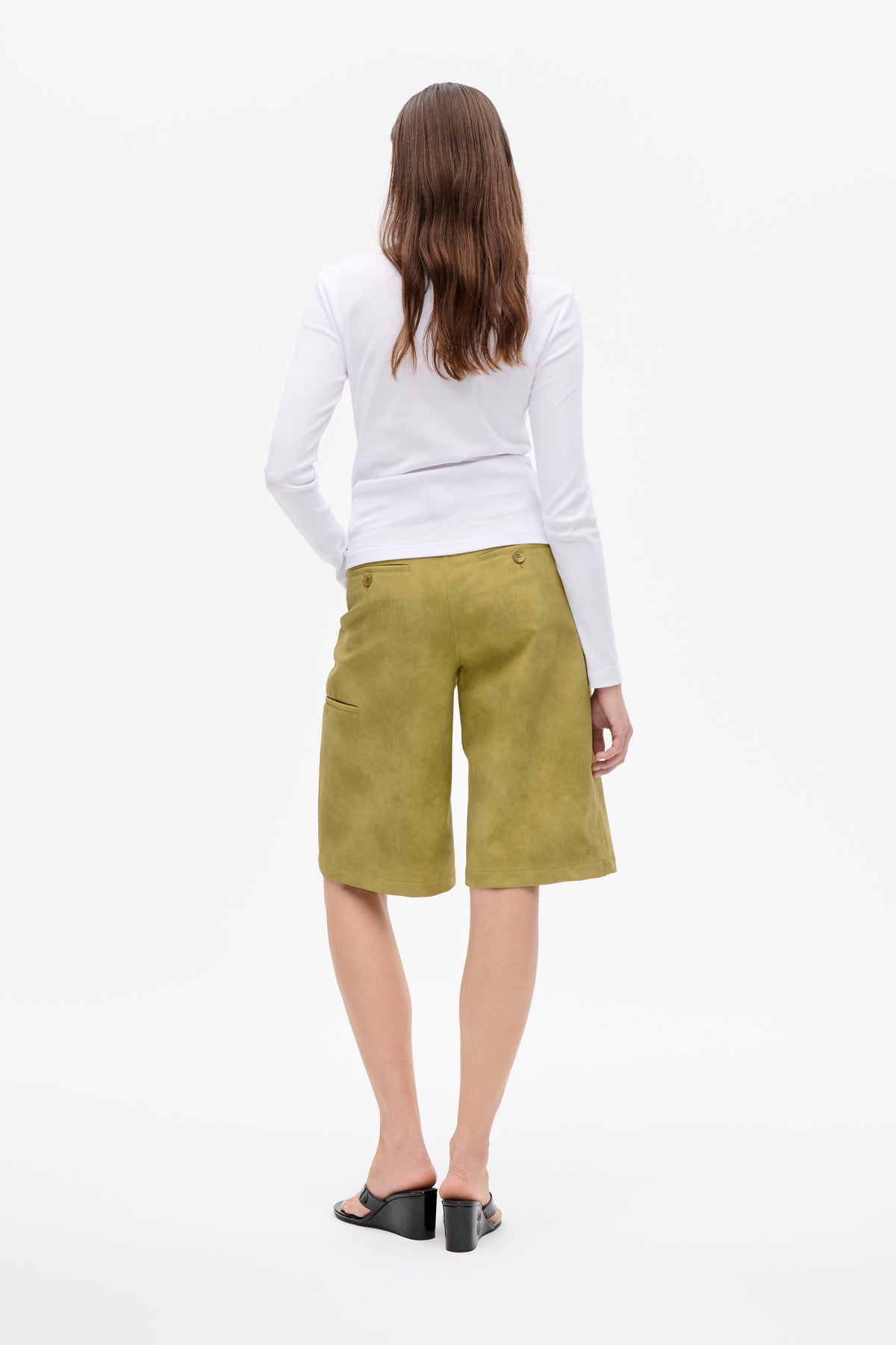 Back view of a model wearing a plain white long-sleeve top and olive-green knee-length wide-leg shorts with rear welt pockets.