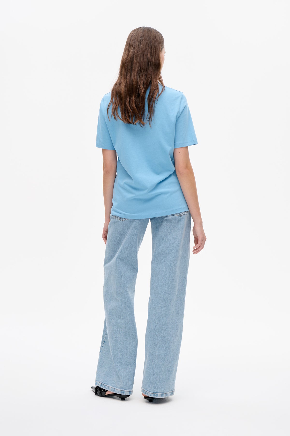 Vue arrière d'un mannequin portant un t-shirt uni bleu clair à manches courtes et un jean à jambe large délavé clair.