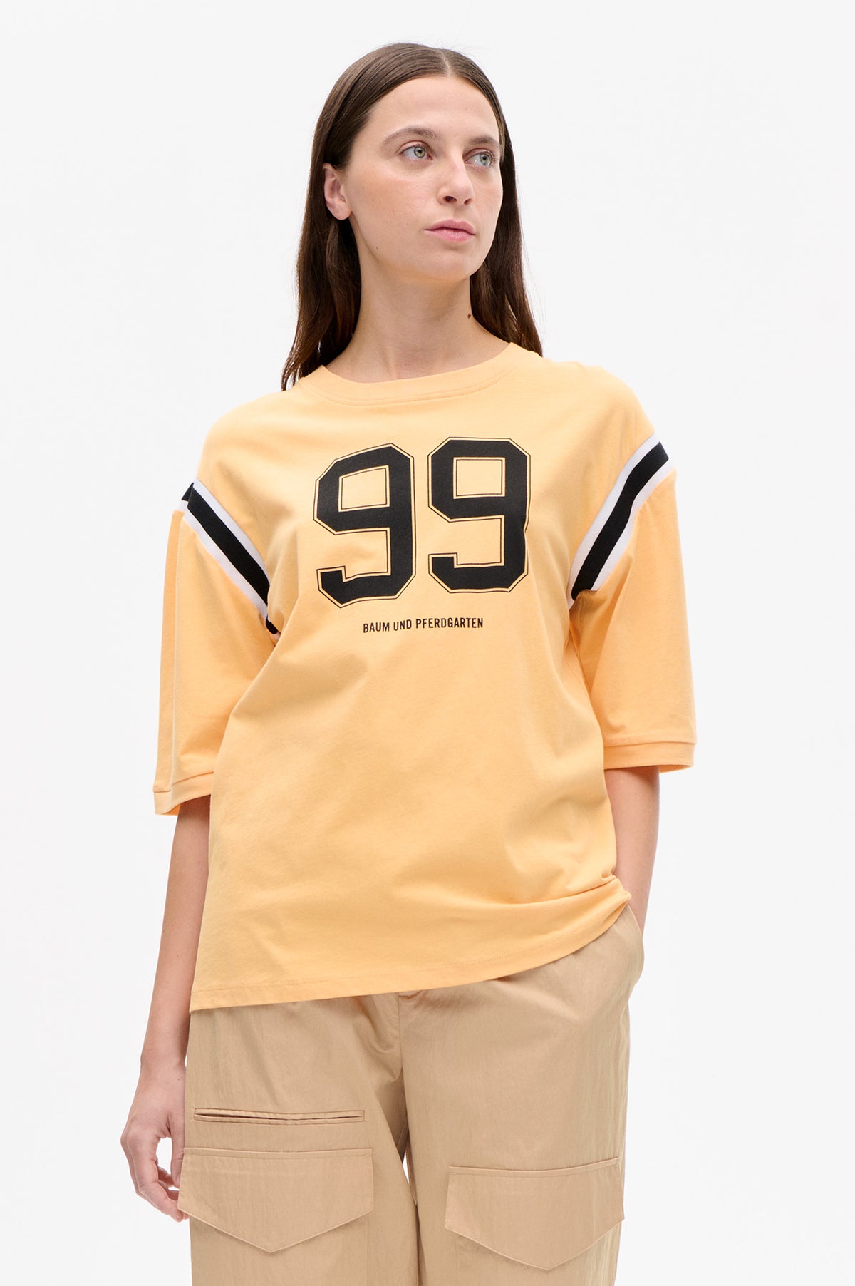 Front detail of a pale yellow short-sleeved T-shirt with a large outlined 99 graphic and black-and-white sleeve stripes.