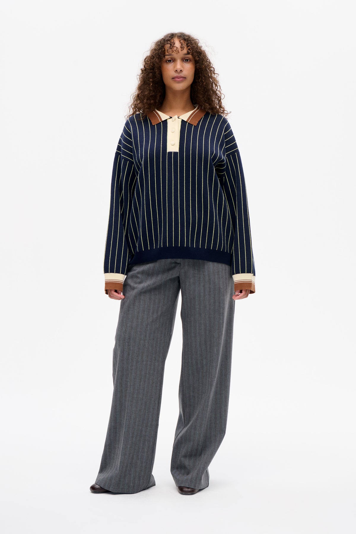 Front view of a navy long-sleeve knit top with thin cream vertical stripes, a brown-and-cream polo collar, button placket and contrast cuffs.