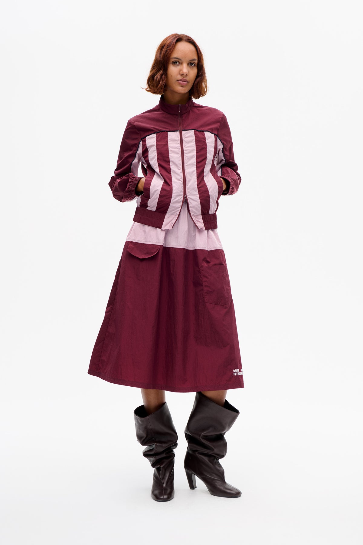 Model wearing a burgundy zip-front jacket with pale pink and burgundy vertical stripes over a matching colour-block midi dress.