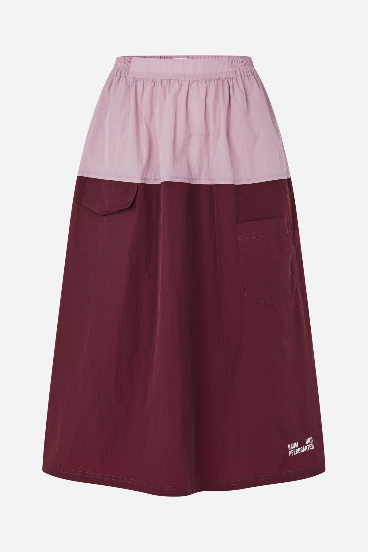 Front view of a long two-tone skirt with a pale pink gathered waistband panel, burgundy A-line body, patch pockets and a small hem logo.