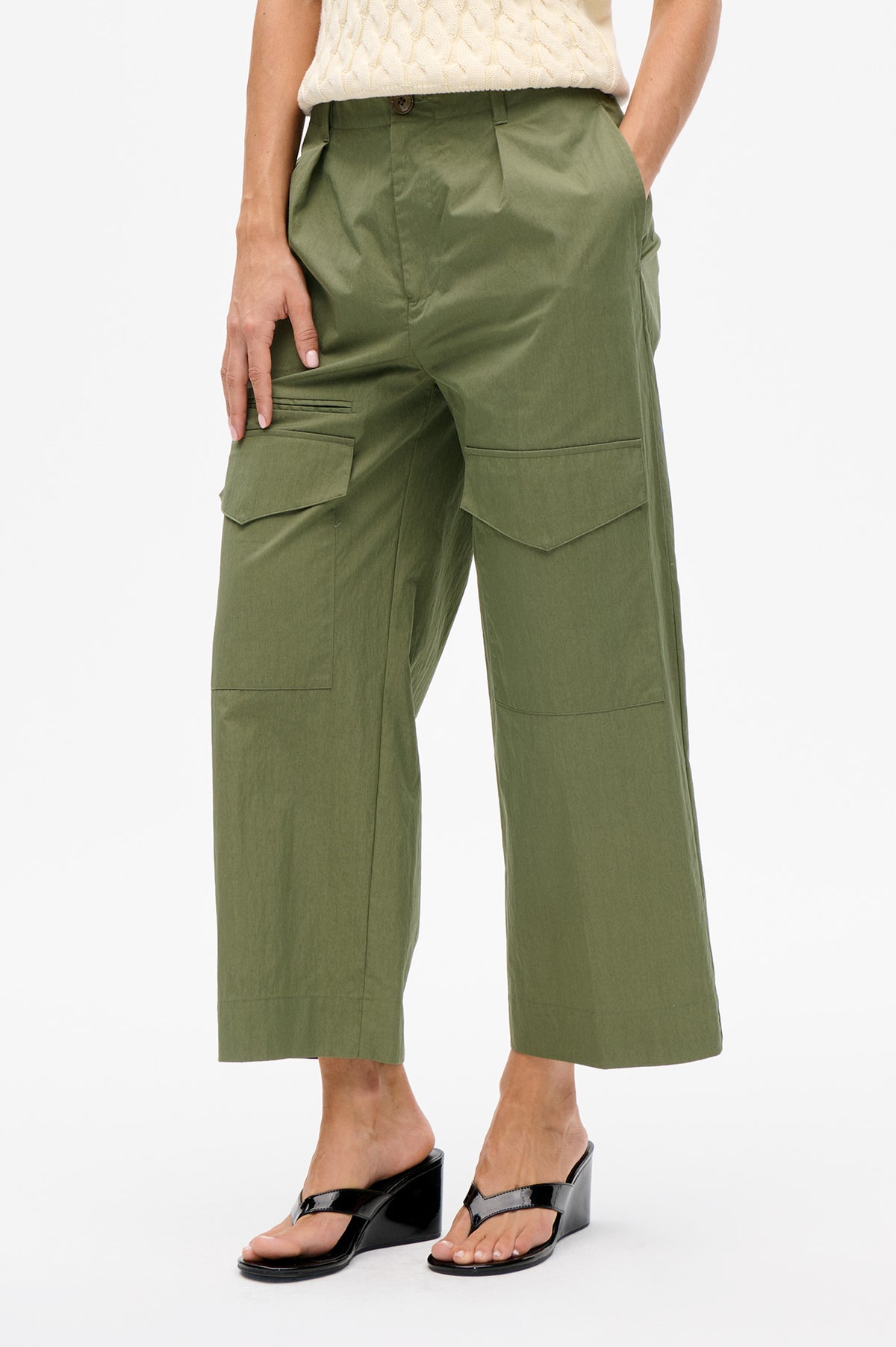 Front detail of olive green wide-leg cropped trousers with oversized flap cargo pockets, styled with a cream cable-knit top.