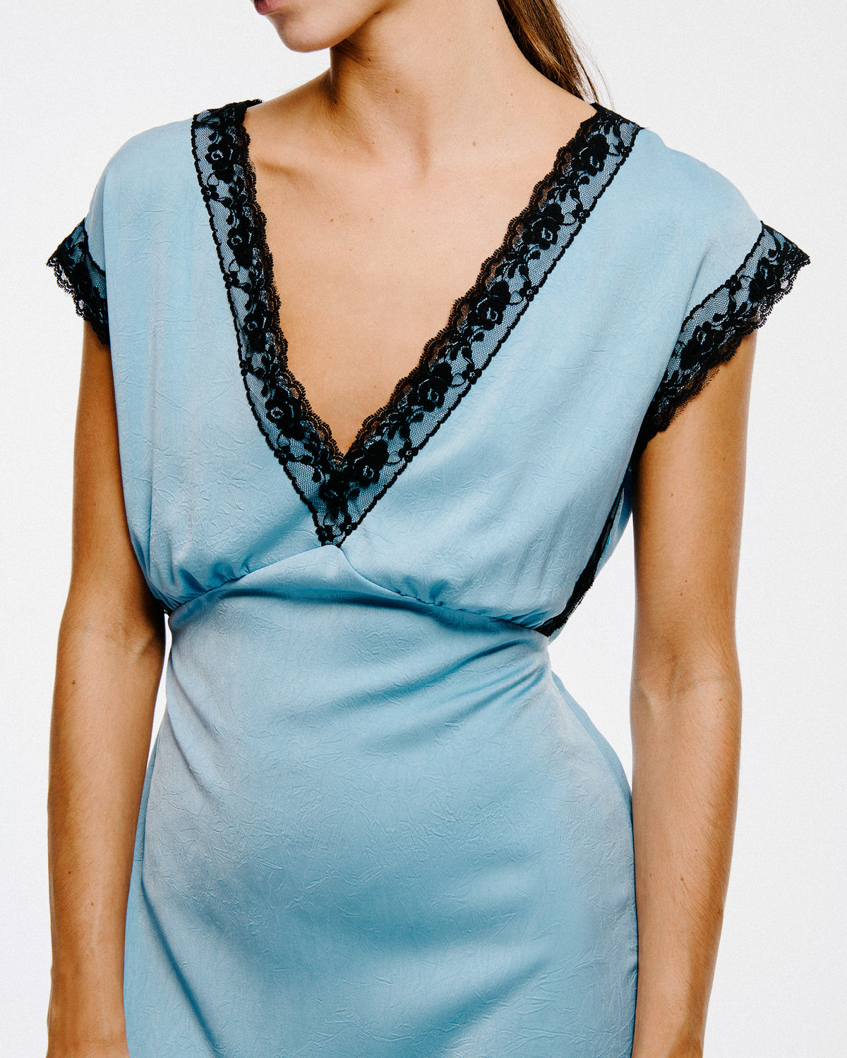 Close-up of a light blue crinkled dress with a deep V-neck and black floral lace trim along the neckline and short sleeves.