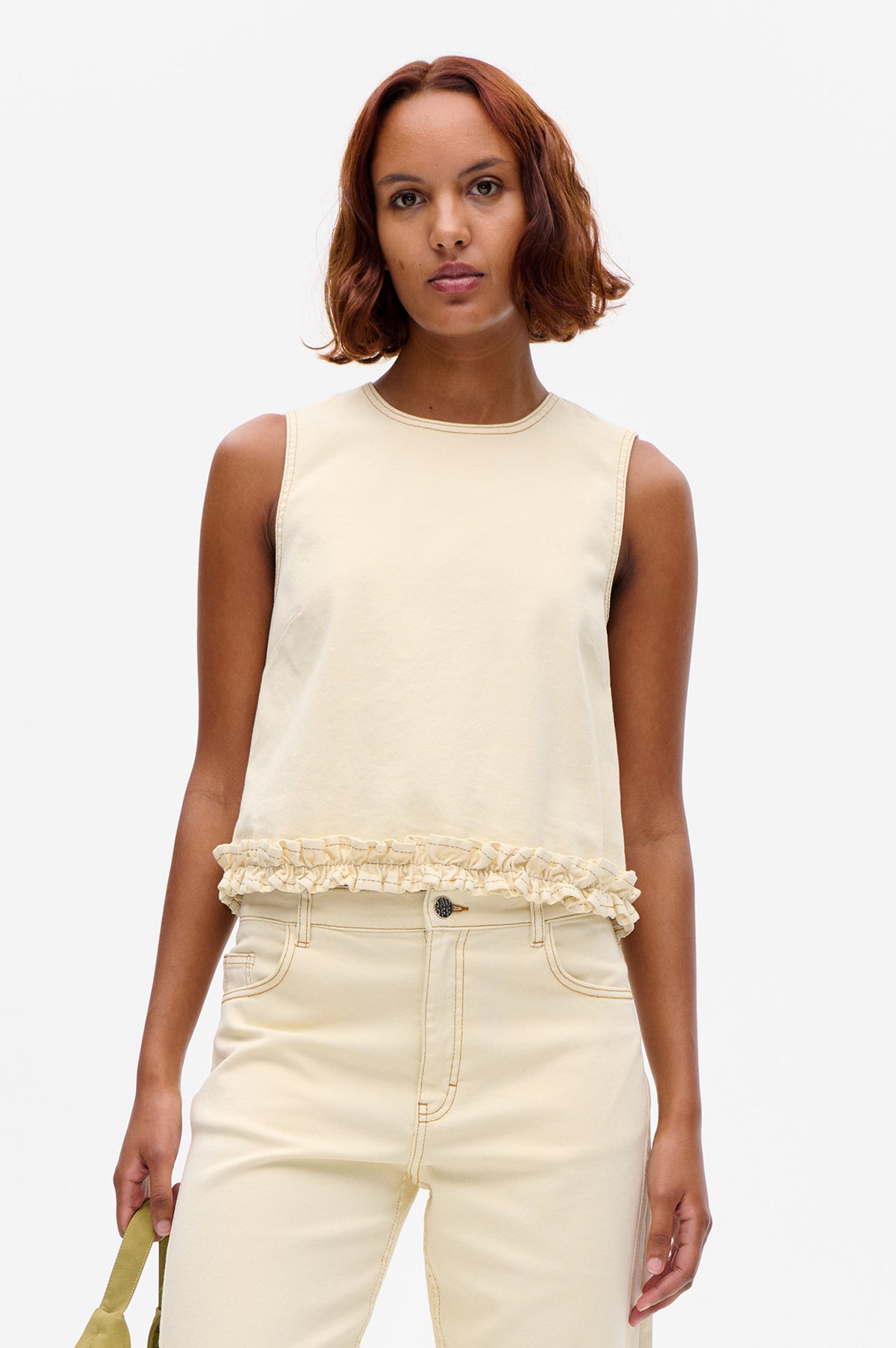 Front view of an ivory sleeveless top with contrast neckline stitching and a ruffled hem, paired with matching trousers.