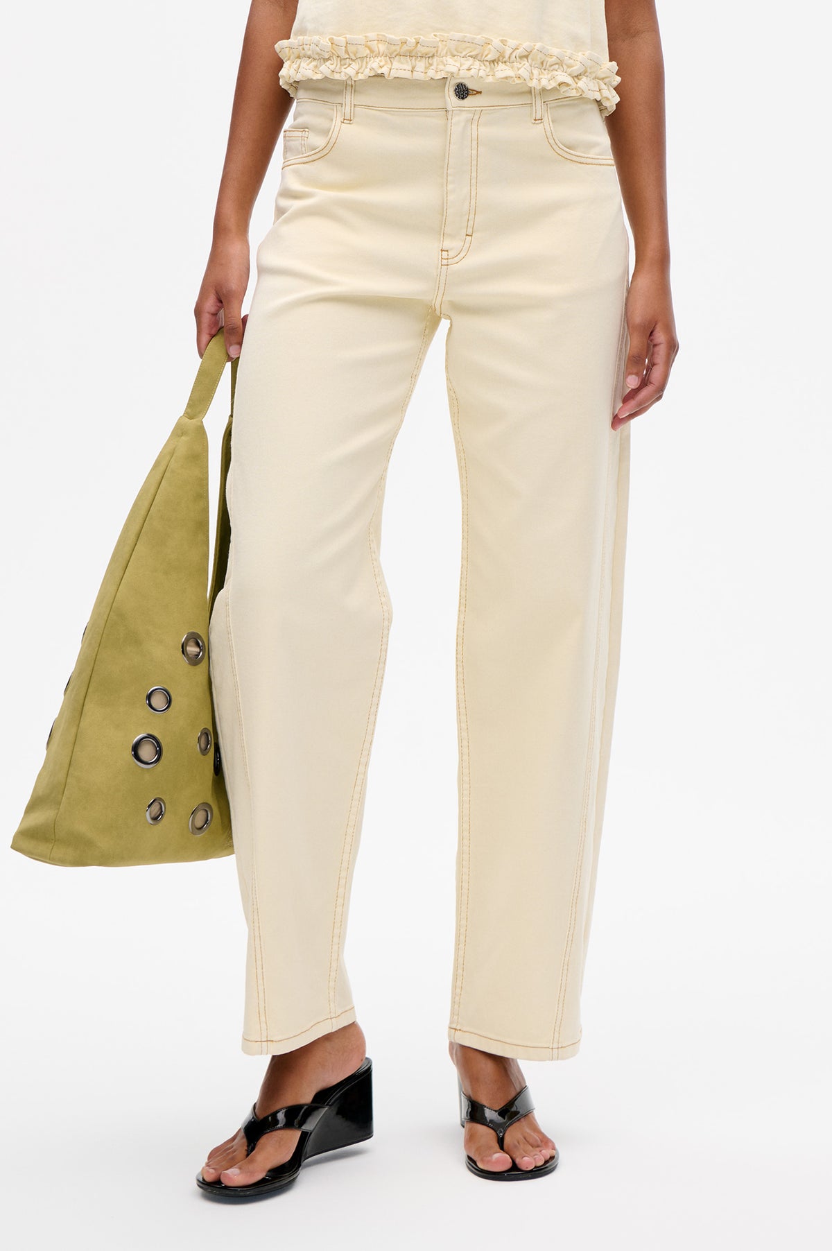 Front detail of cream cropped jeans with contrast stitching and a ruffled hem top, styled with an olive bag and black sandals.