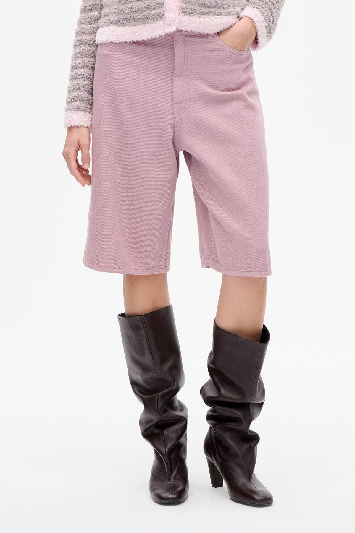 Close-up of a model wearing dusty pink cropped wide-leg trousers with a front pocket and dark brown knee-high boots.