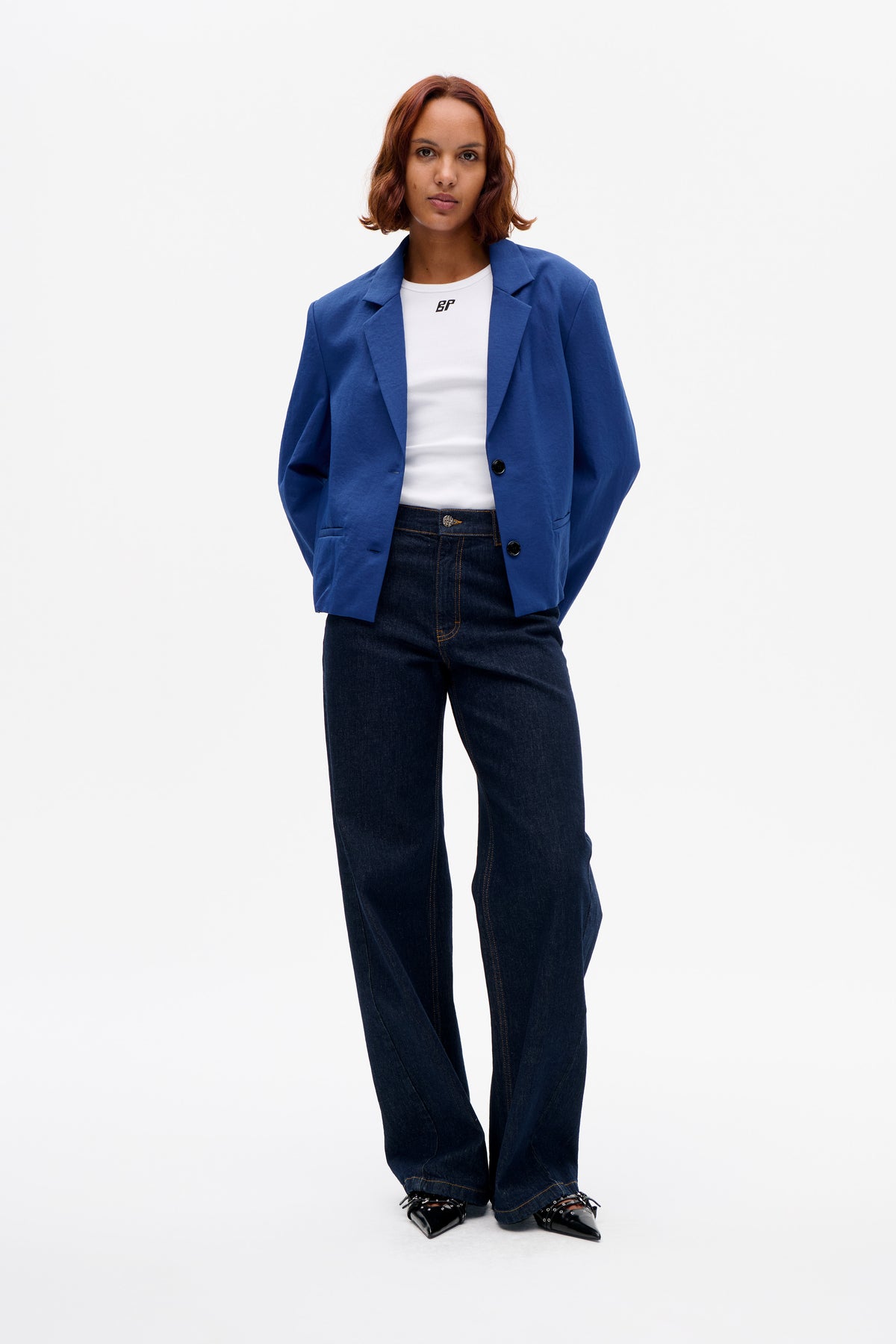 Model wearing a cobalt blue button-front blazer, white T-shirt with a small BP logo, and dark wide-leg jeans