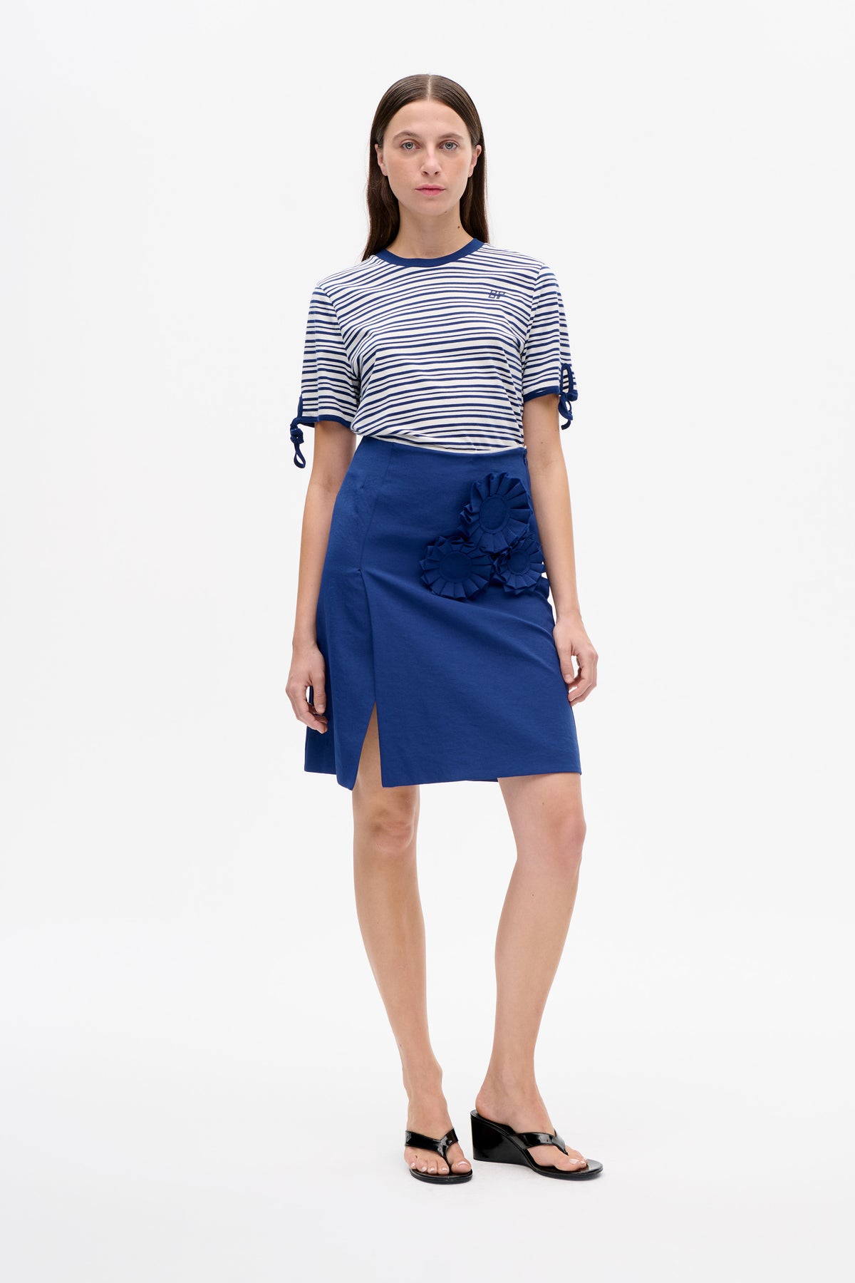 Model trägt ein weiß- und marineblau gestreiftes T-Shirt mit Bindebandärmeln und einen kobaltblauen Rock mit floralen Applikationen und vorderem Schlitz.