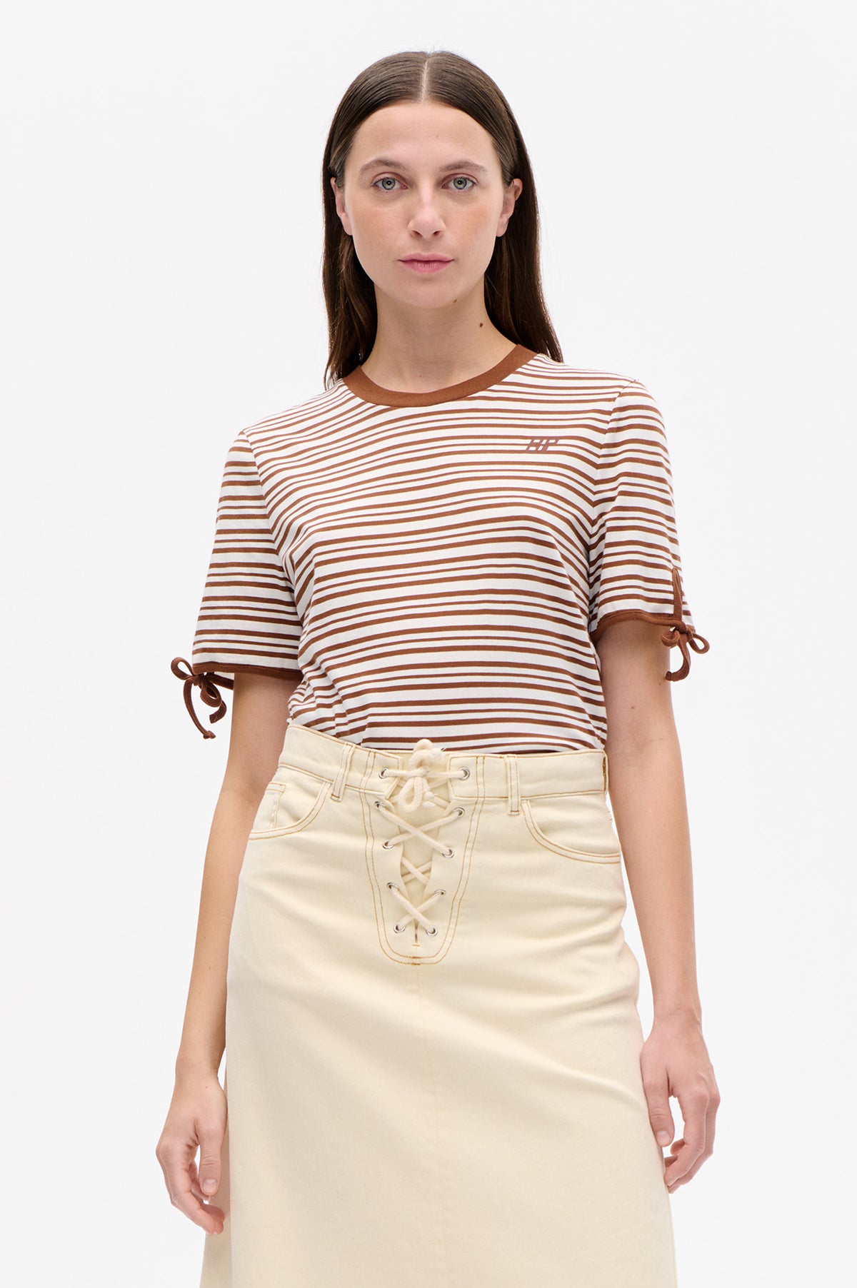 Front view of a white T-shirt with brown stripes, brown neckline and sleeve ties, worn with a cream lace-up skirt.