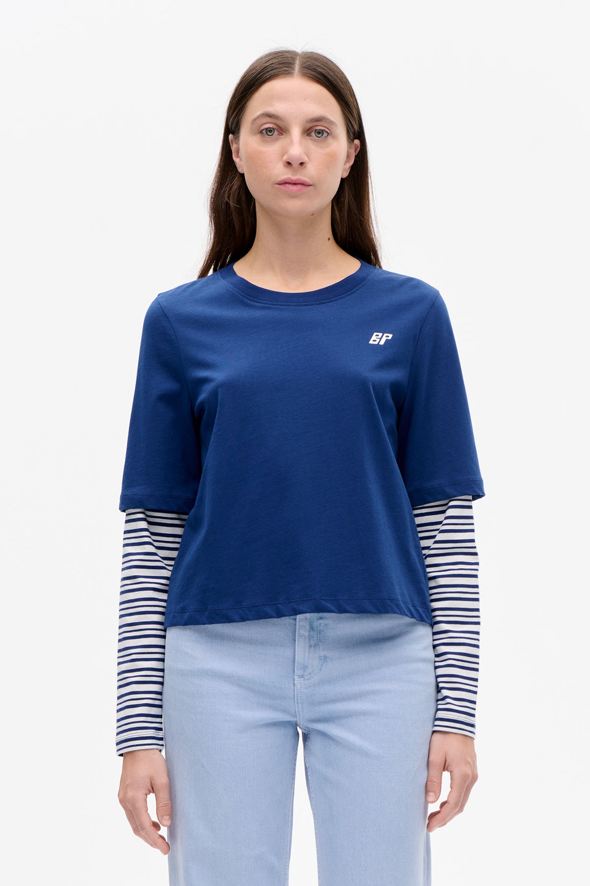 Model wearing a blue short-sleeve T-shirt with a small white BP chest logo over a navy-and-white striped long-sleeve top and light-wash jeans.
