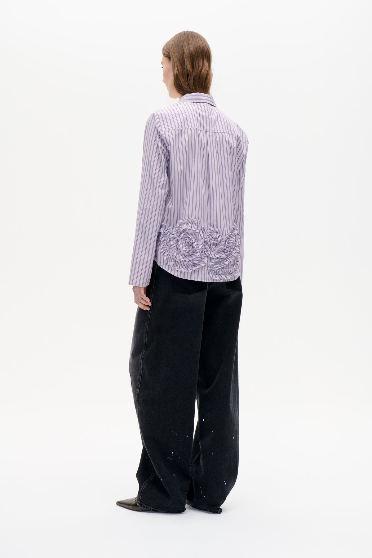 Back view of a pale lavender pinstriped collared shirt with long sleeves and gathered ruffle detailing across the lower back.