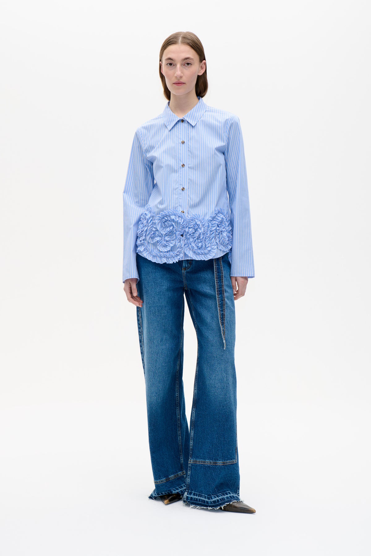 Front view of a model wearing a blue-and-white striped button-front shirt with a ruffled lower panel and wide-leg blue jeans.