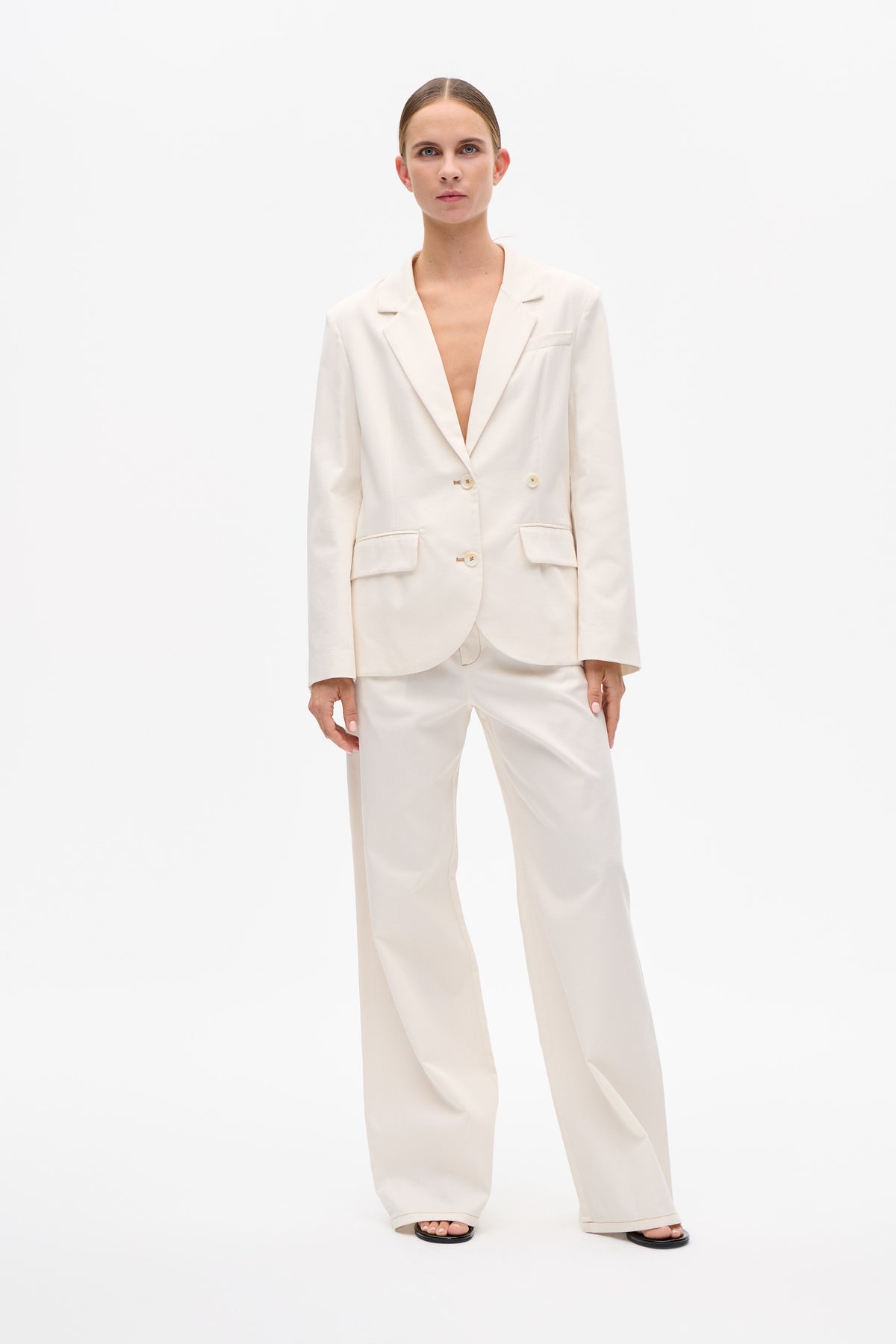 Front view of a model wearing an ivory double-breasted blazer with notch lapels and patch pockets, paired with wide-leg trousers.