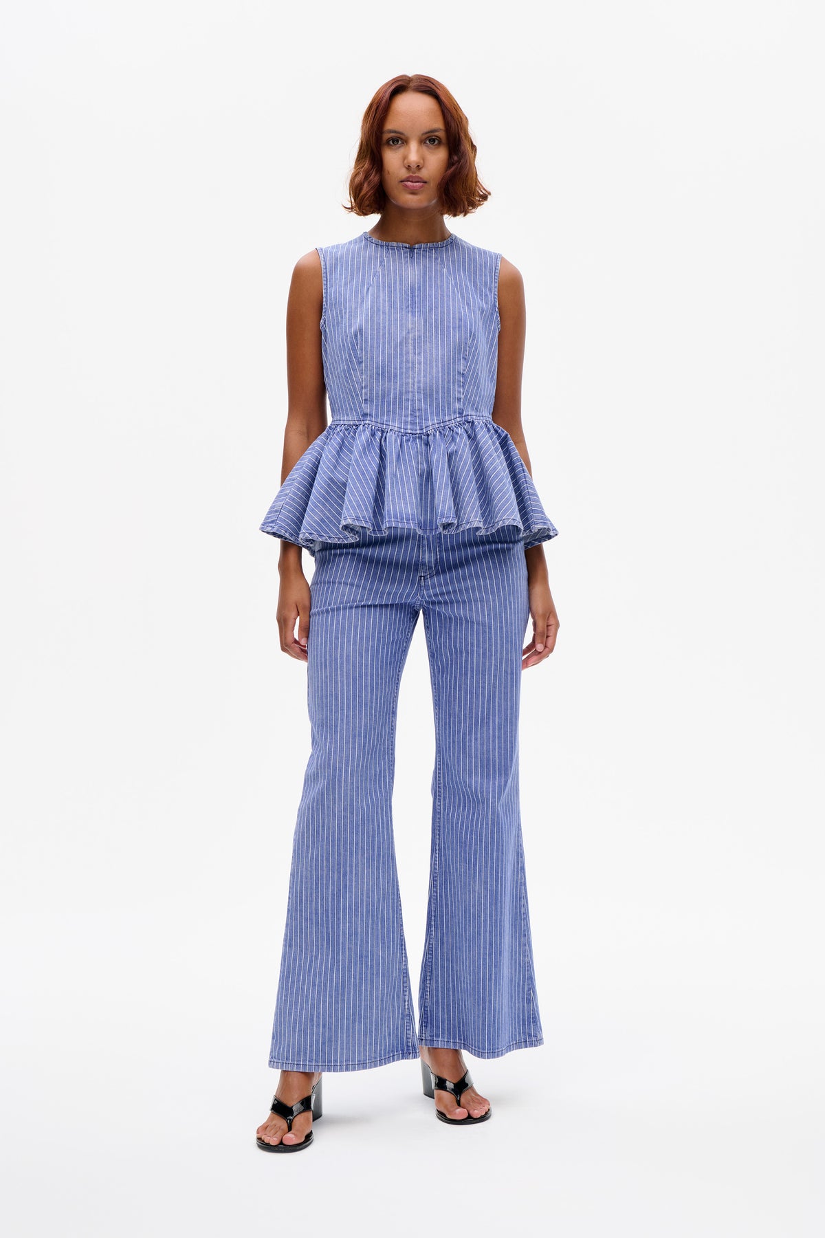 Front view of a blue-and-white pinstriped sleeveless top with a high neckline and flounced peplum, worn with matching wide-leg trousers.
