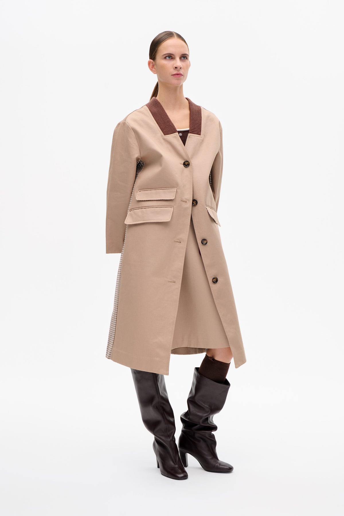 Model wearing a beige long coat with a ribbed brown V-shaped collar, button front, patch pockets and checked trim.
