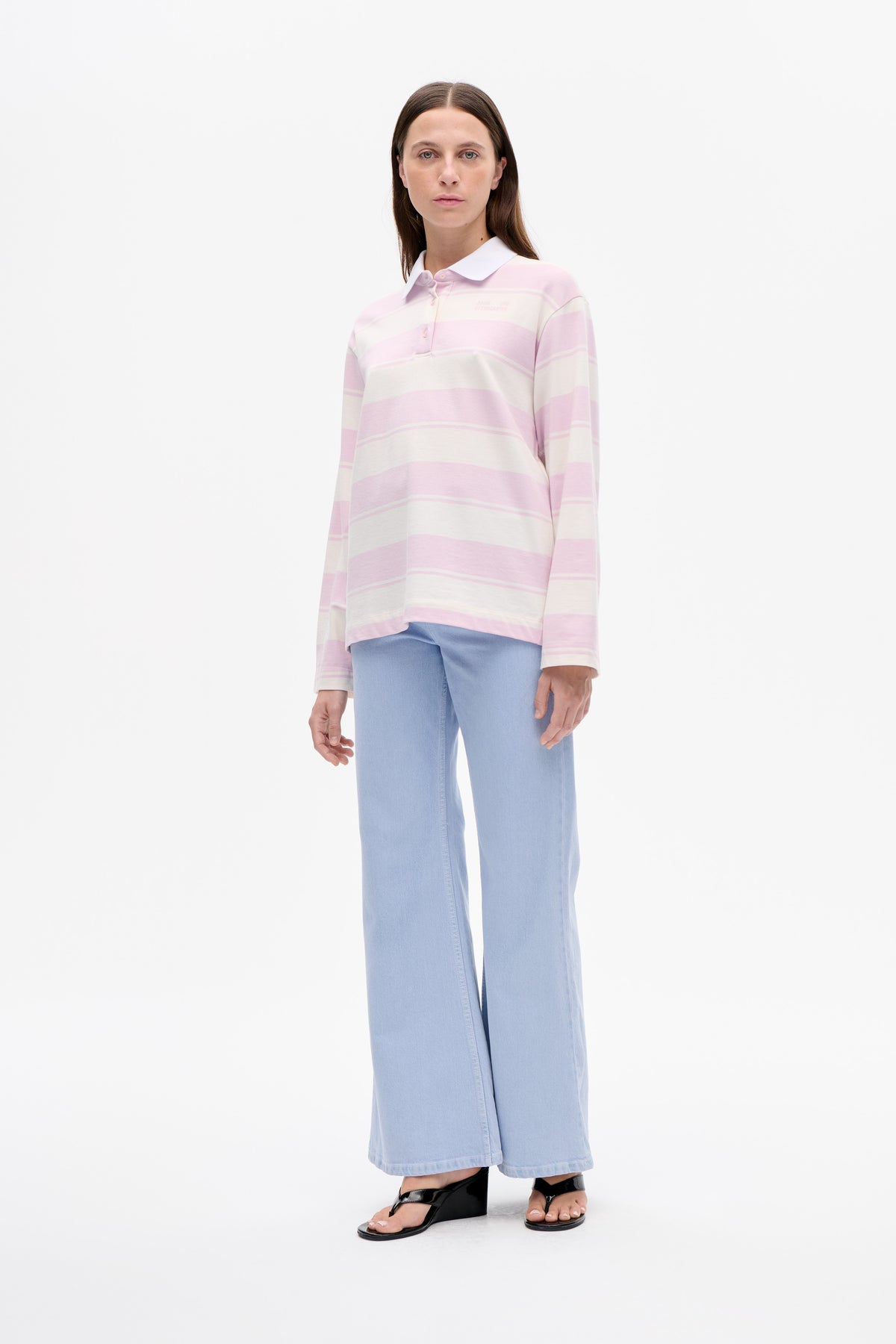 Model van voren draagt een roze‑crème gestreept poloshirt met lange mouwen en witte kraag, gecombineerd met lichtblauwe wide‑leg jeans.
