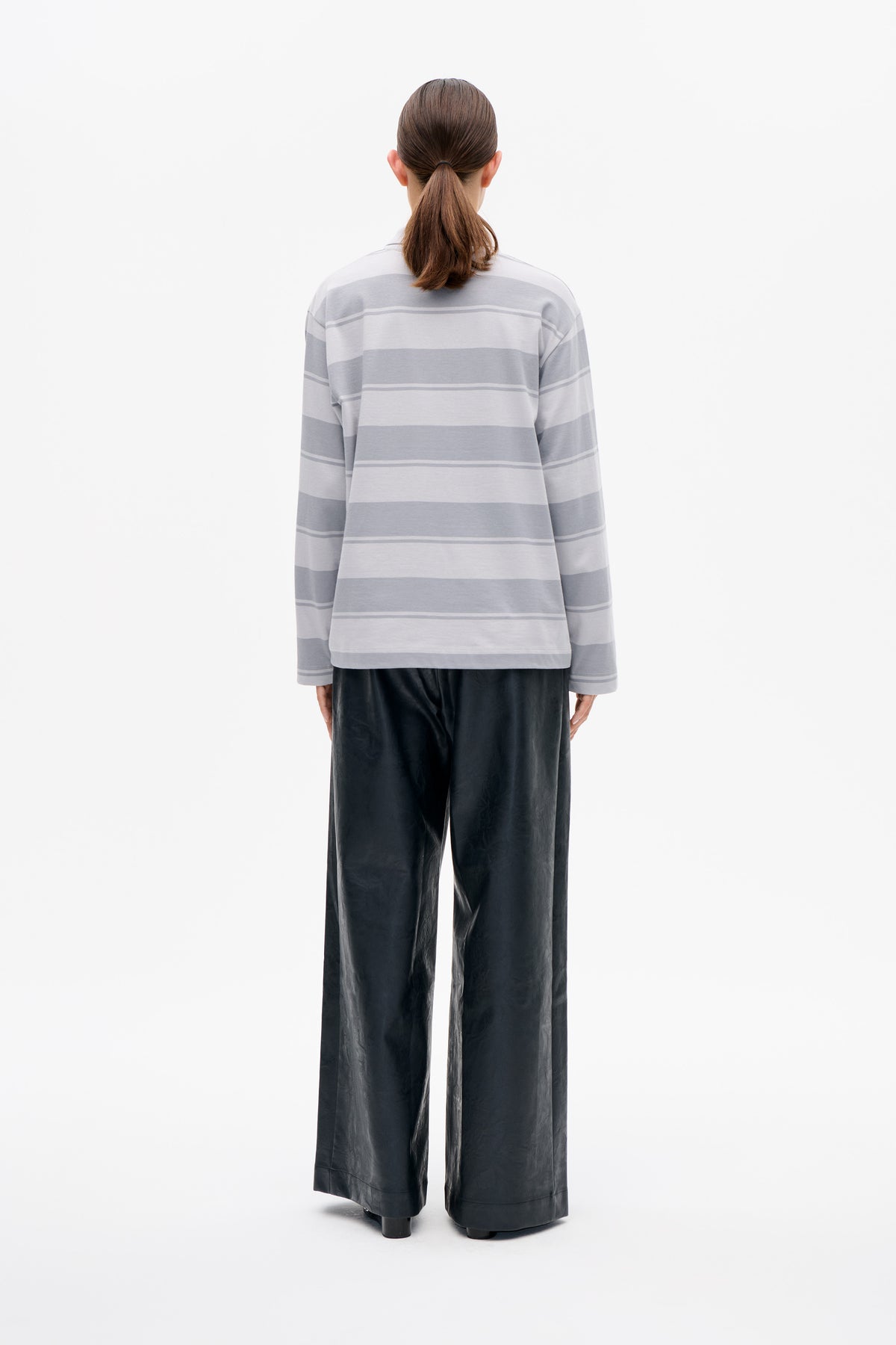 Back view of a model wearing a long-sleeved top with broad grey and white horizontal stripes and black wide-leg trousers.