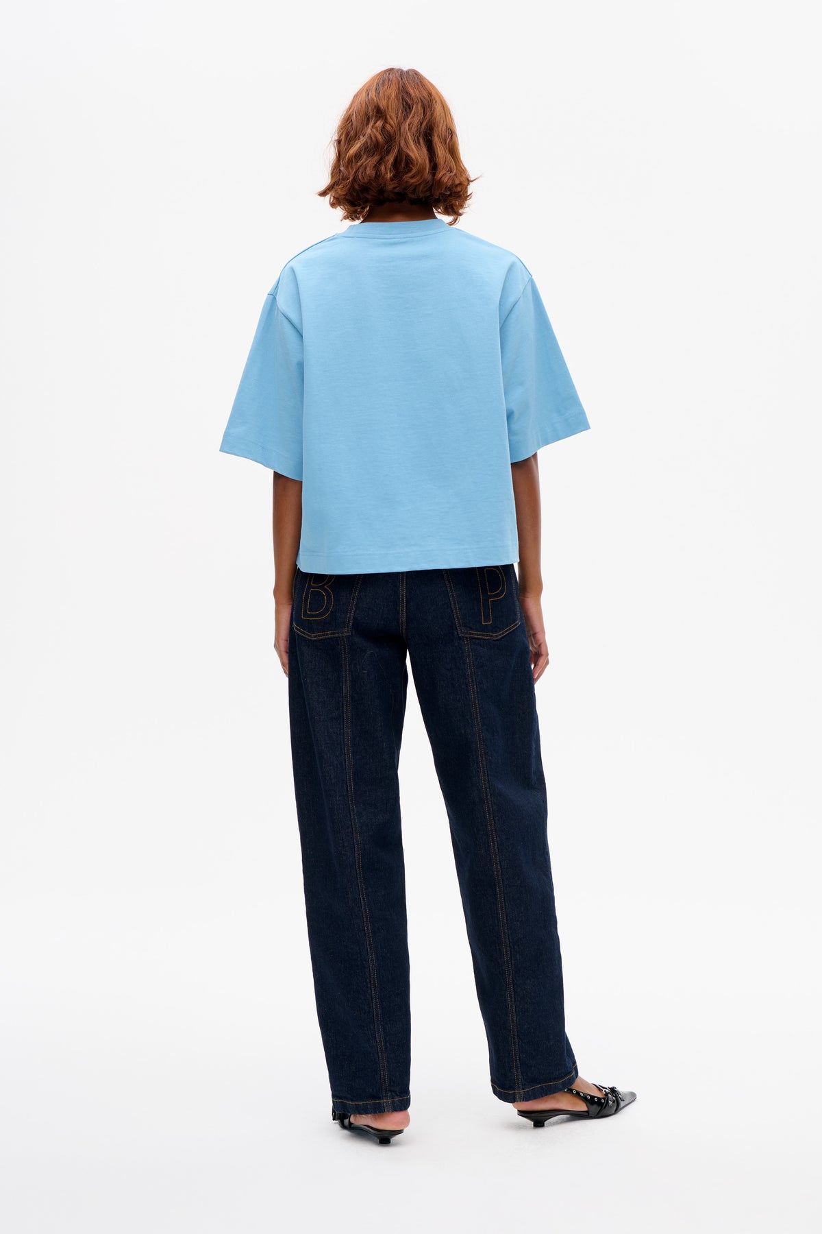 Vue de dos d'un t-shirt bleu clair oversized à manches courtes, porté avec un jean large indigo foncé aux poches arrière ornées d'un lettrage en contour.
