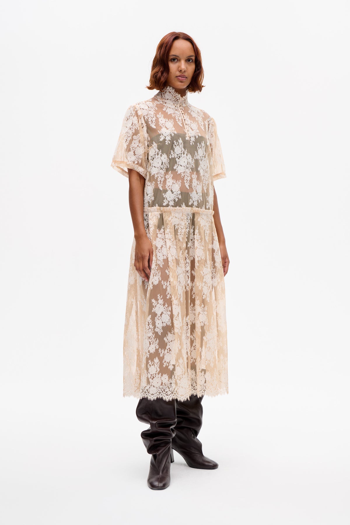 Model wearing a sheer ivory floral lace dress with a high neck, short sleeves and a gathered skirt, front view