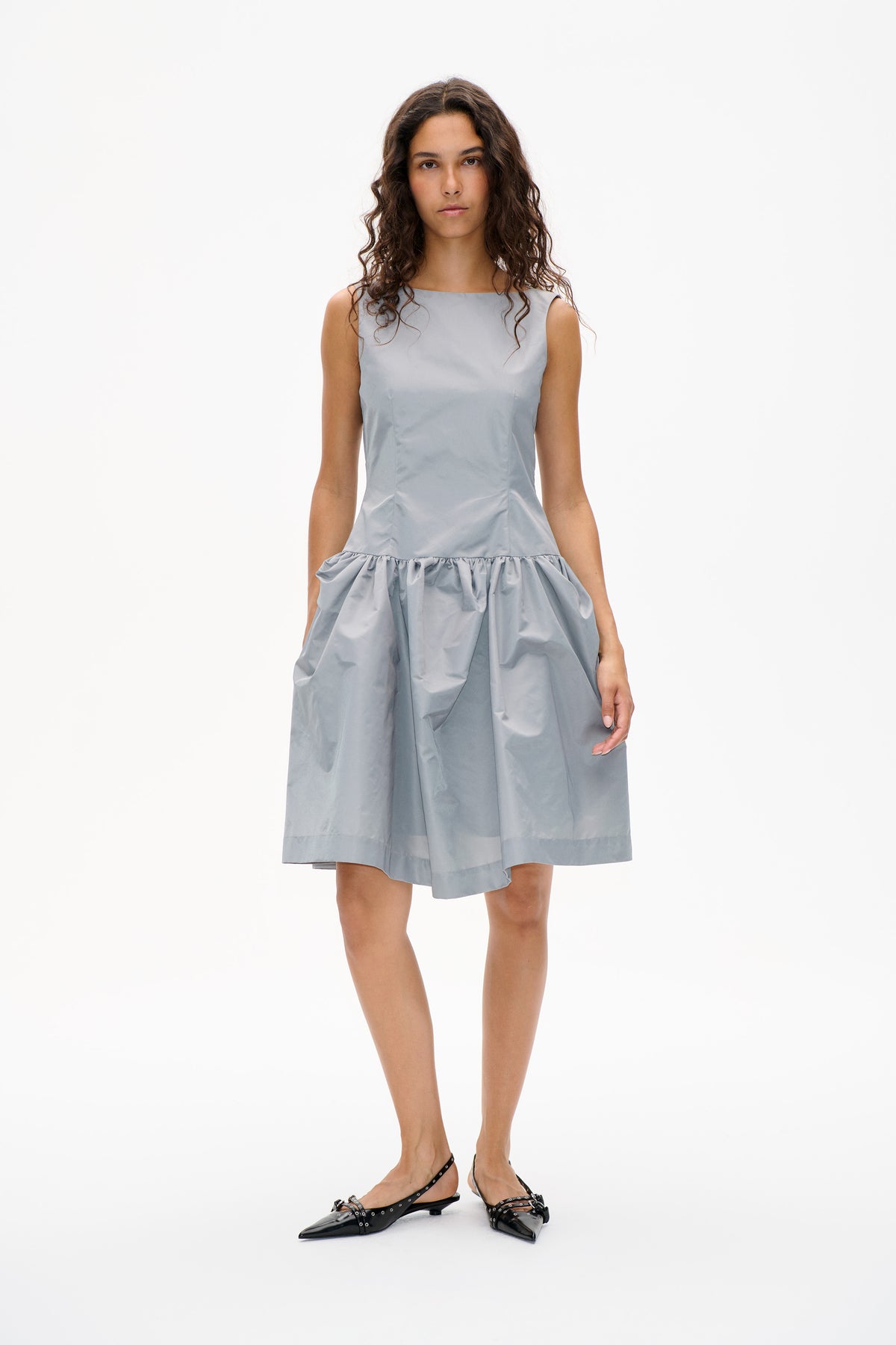 Model wearing a pale blue-gray sleeveless dress with a fitted bodice and gathered, voluminous knee-length skirt, shown from the front.