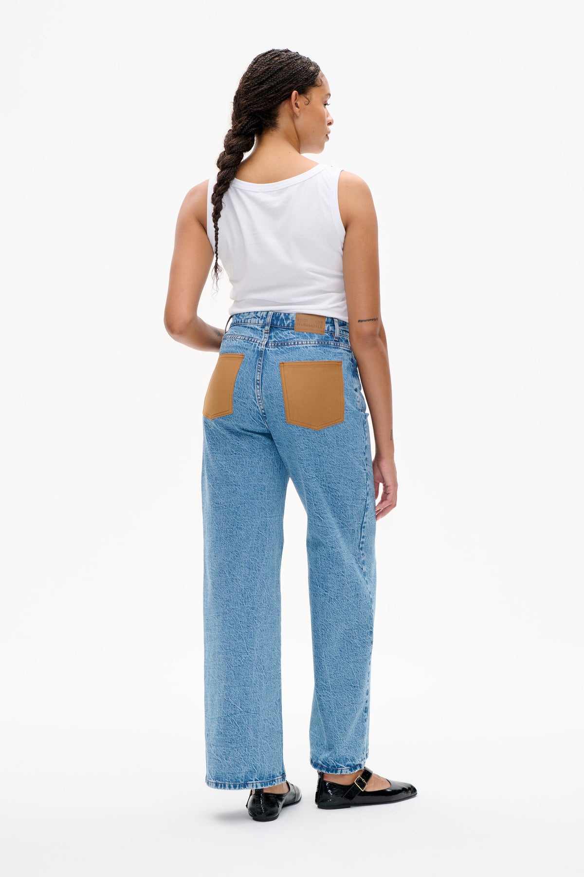 Achteraanzicht van lichtblauwe jeans met oversized lichtbruine opgestikte zakken, gestyled met een witte mouwloze top en zwarte flats.