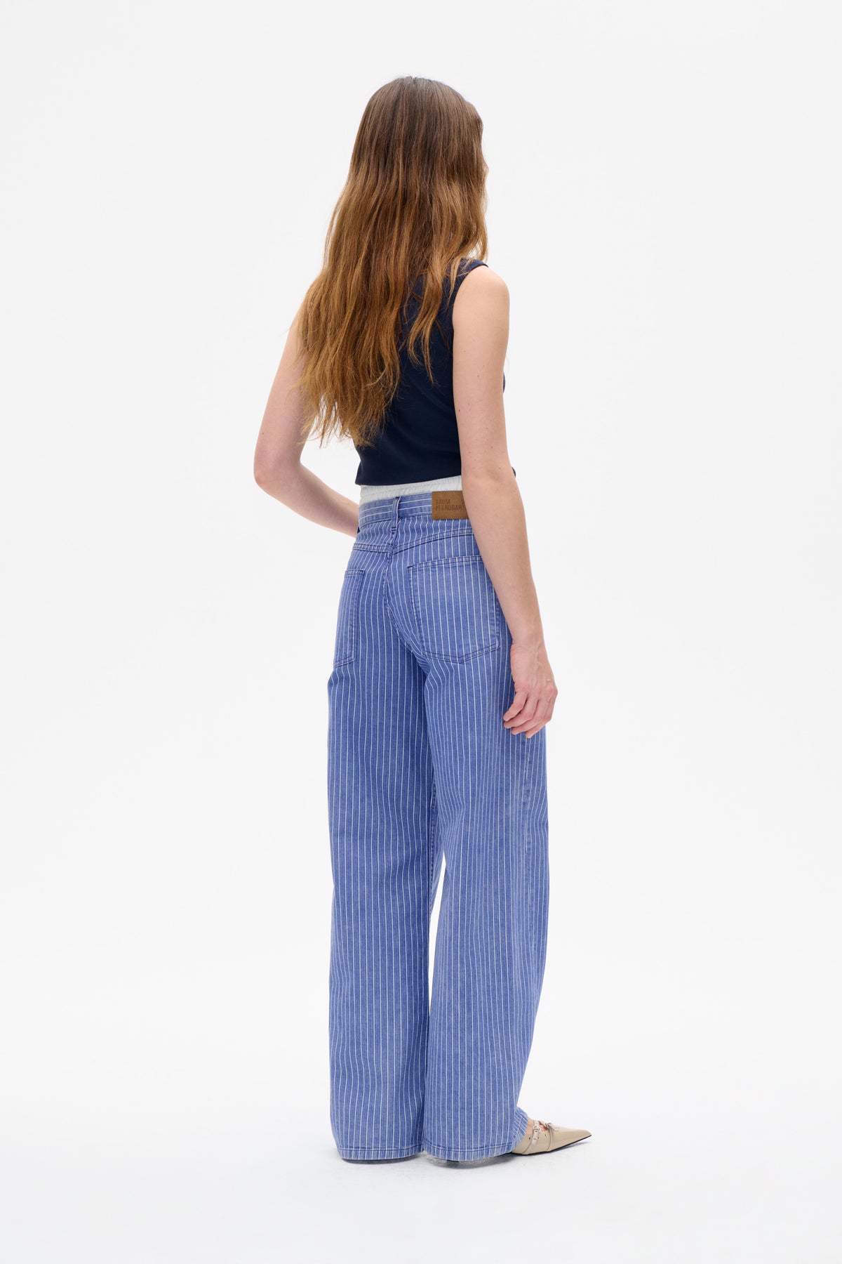 Rückenansicht eines Models in einem marineblauen ärmellosen Top und einer blauen, weit geschnittenen Hose mit feinen weißen Nadelstreifen und Gesäßtaschen.
