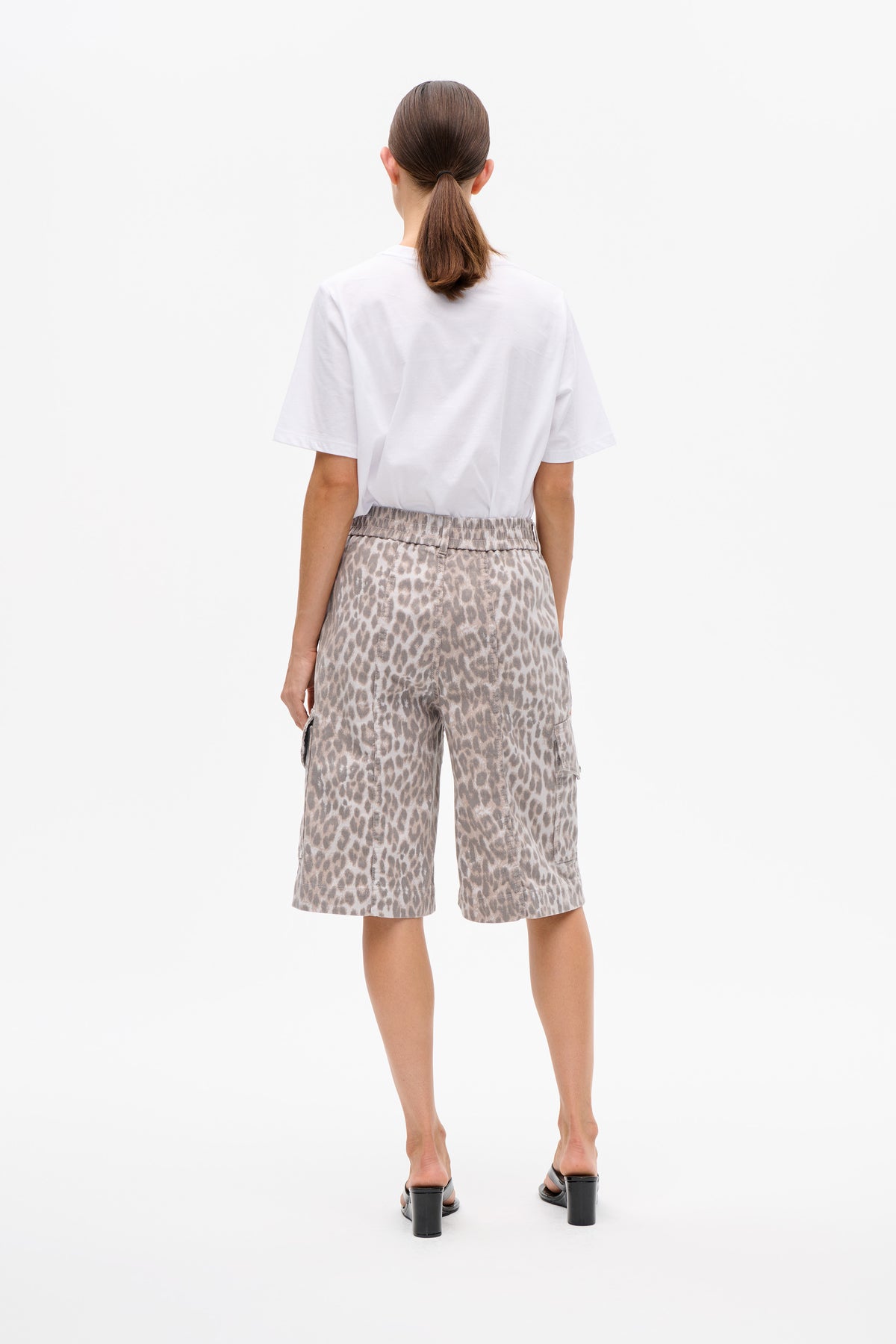 Model van achteren gezien in een witte T-shirt met korte mouwen en losse taupekleurige cargo-shorts met dierenprint en een elastische tailleband.