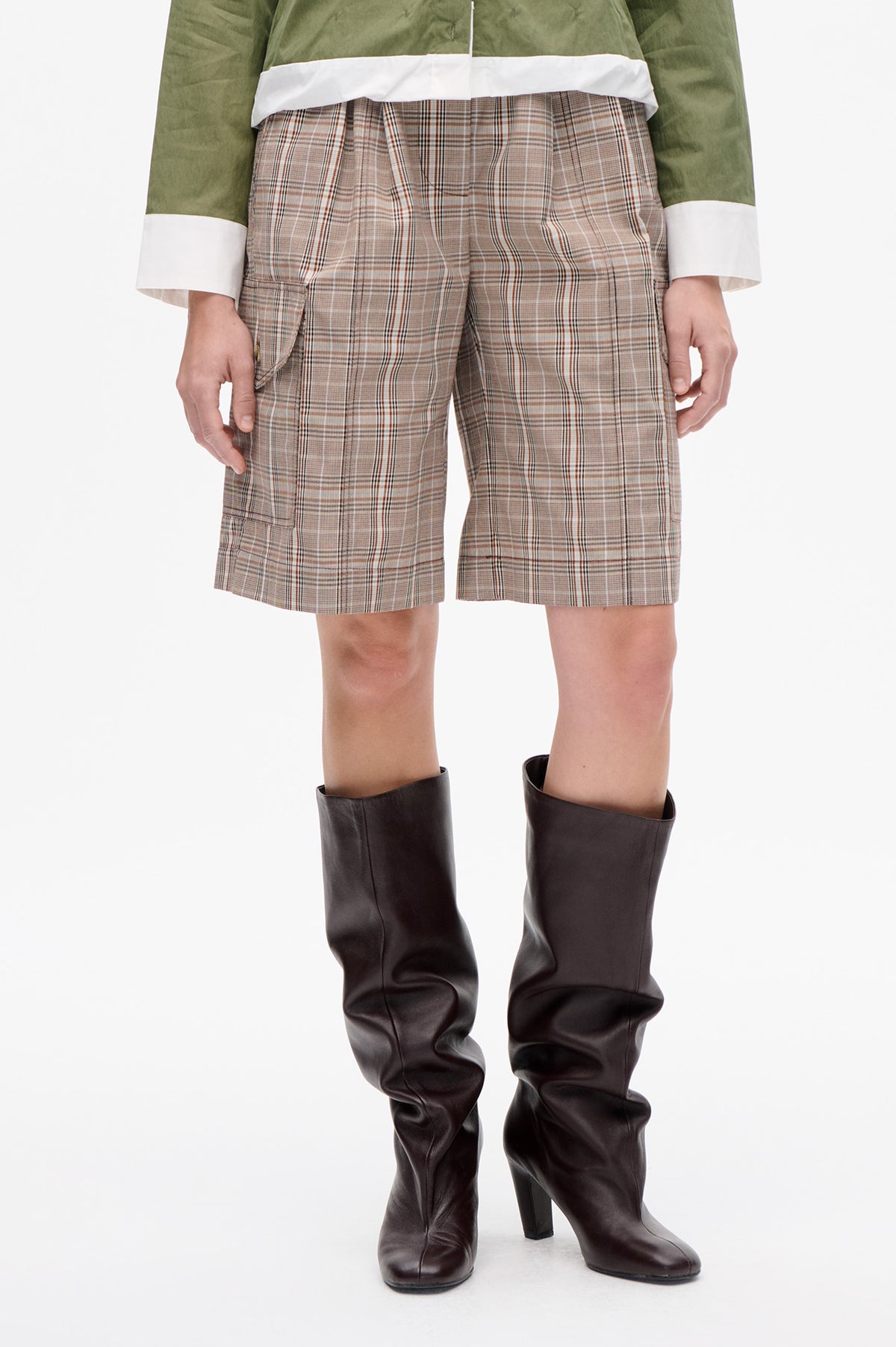 Front detail of beige plaid knee-length shorts with pleats and side pockets, styled with a green top and dark brown boots.
