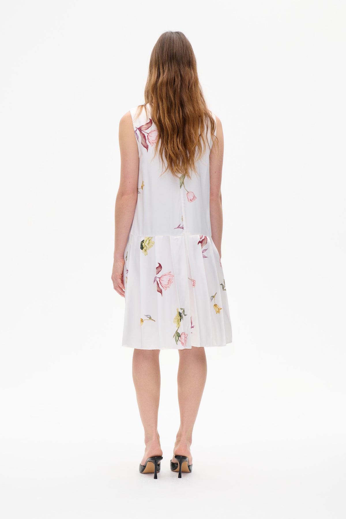 Back view of a white sleeveless knee-length dress with a gathered skirt and scattered pink, burgundy and yellow floral print.